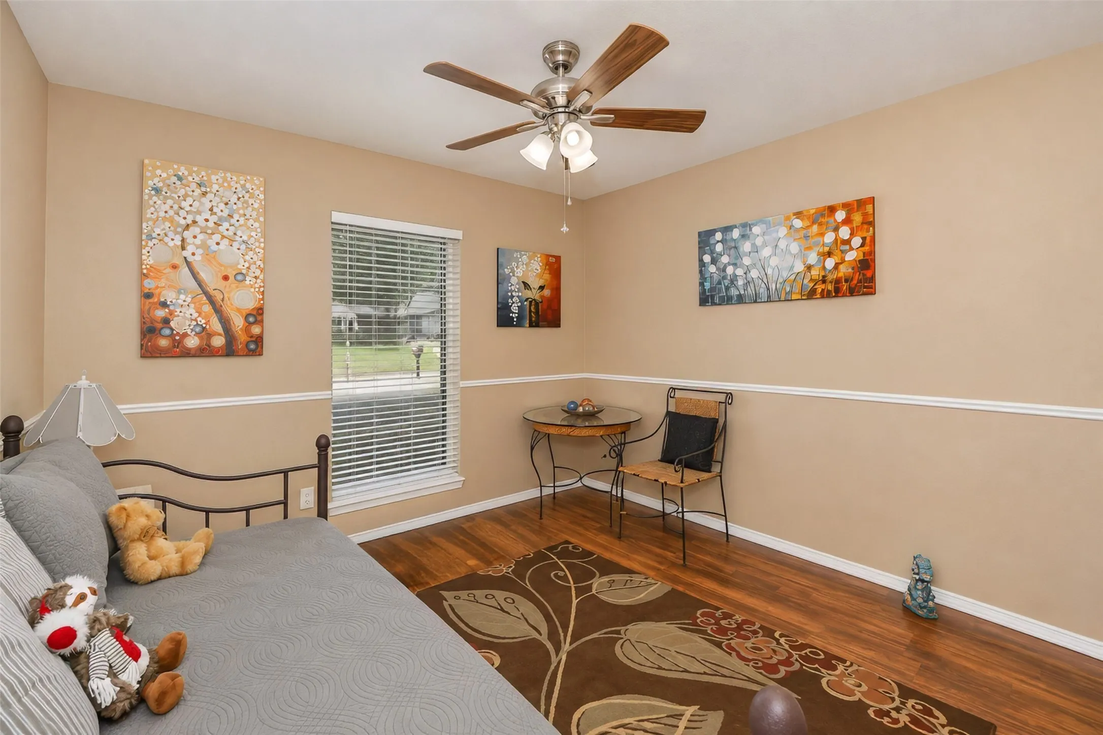 Wood-finish flooring, ceiling fan with light fixture, single window with blinds, and decorative chair rail molding