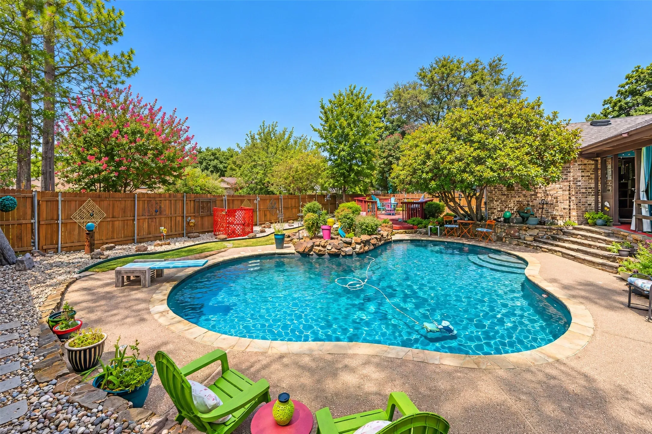 Curved swimming pool with integrated steps, surrounded by a concrete pool deck and stone landscaping