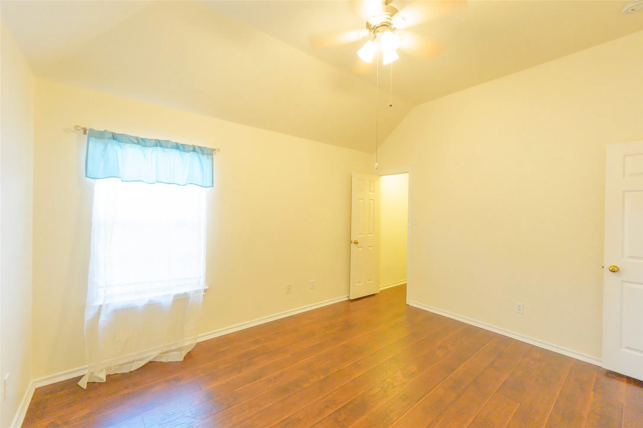 Vaulted ceiling, wood-finish flooring, ceiling fan, white paneled door, window with natural light