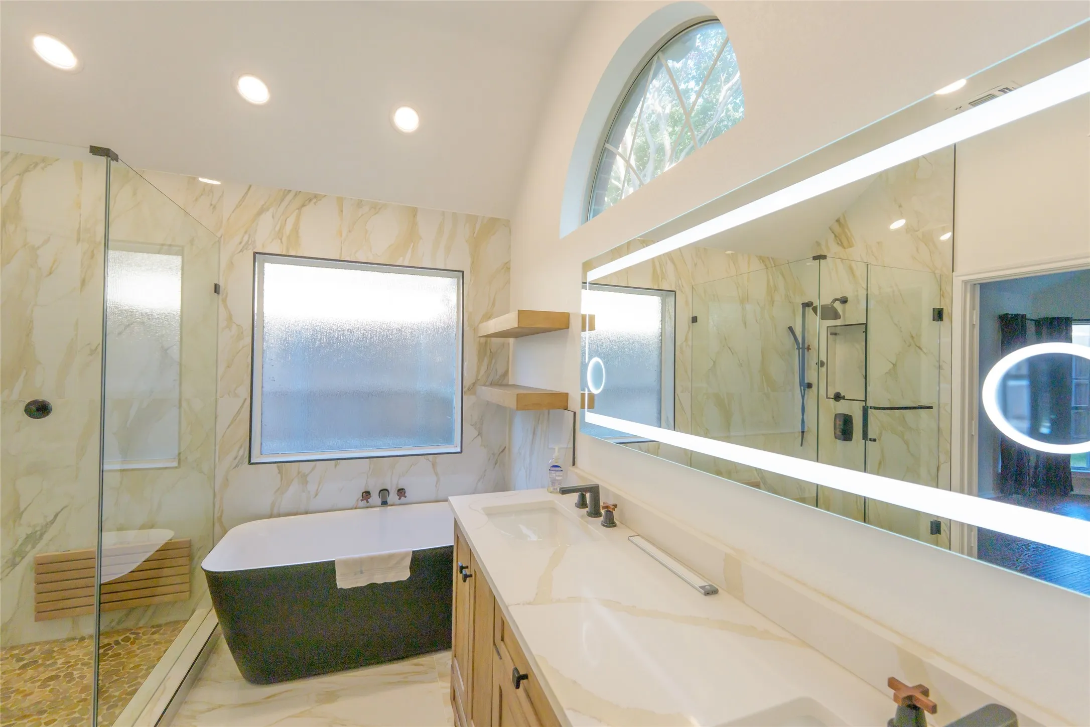 Walk-in shower with a wood-finish bench, freestanding tub, dual vanity with undermount sinks, and an illuminated mirror