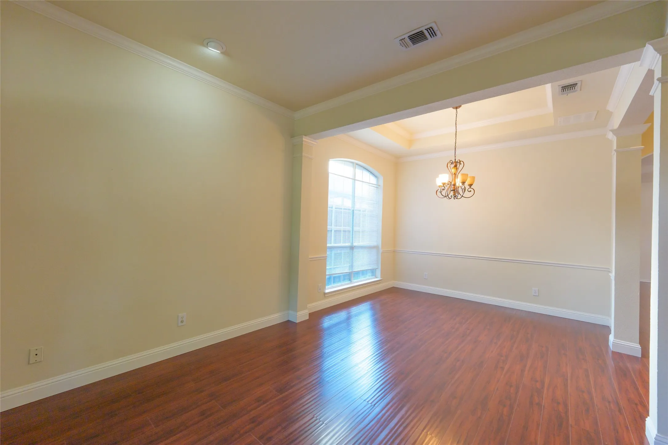 Hardwood-finish flooring, arched window, tray ceiling, decorative chandelier, and crown molding