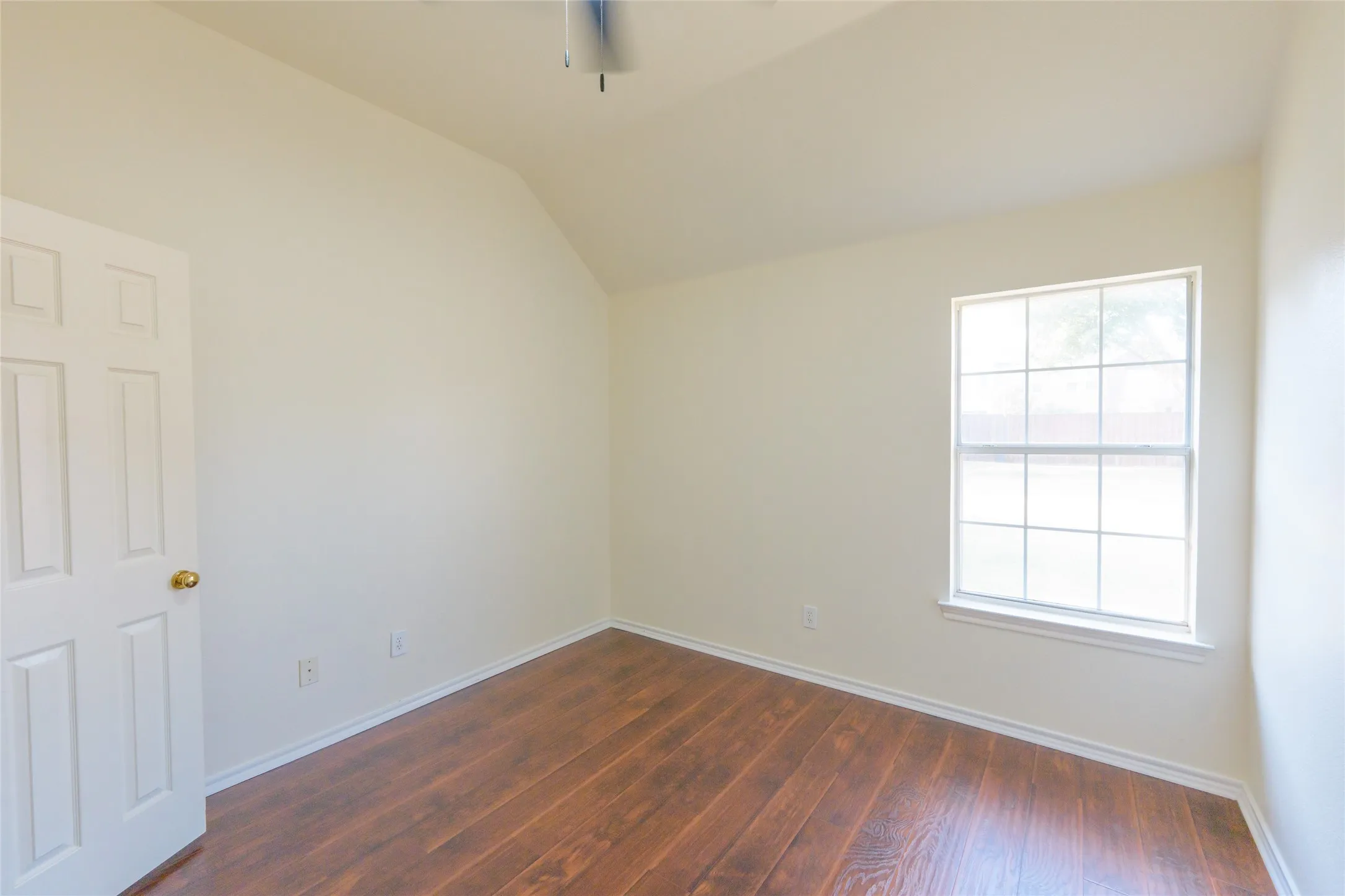 Vaulted ceiling, wood-finish flooring, paneled interior door, window with grid pattern, and neutral wall tones