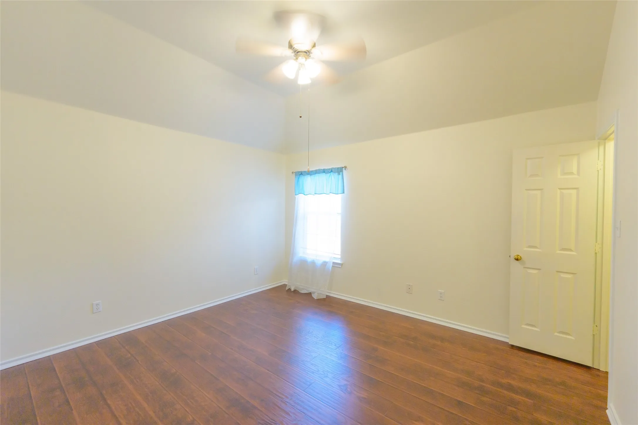 Vaulted ceiling with a ceiling fan, wood-finish flooring, and a single window