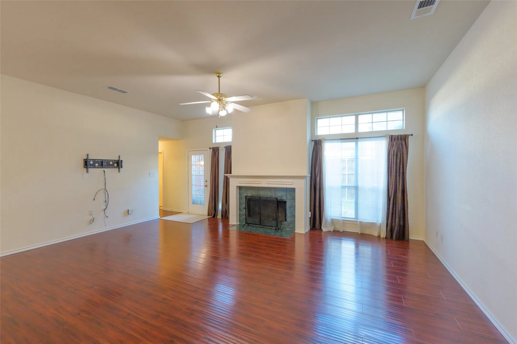 Hardwood-finish flooring, fireplace with a green tile surround, white mantel, and ceiling fan