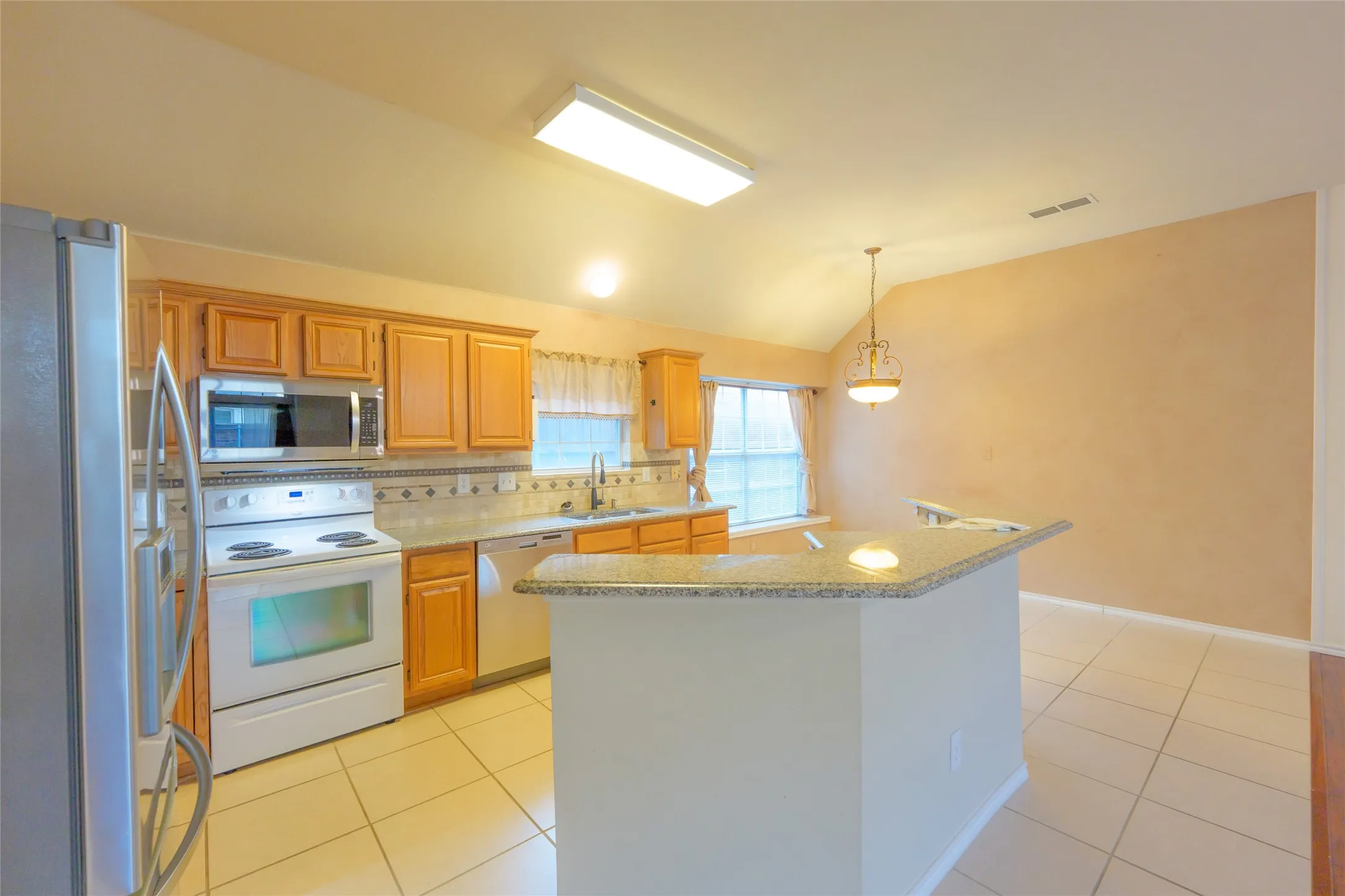 Kitchen featuring a peninsula island, tile flooring, wood-finish cabinetry, and a tile backsplash