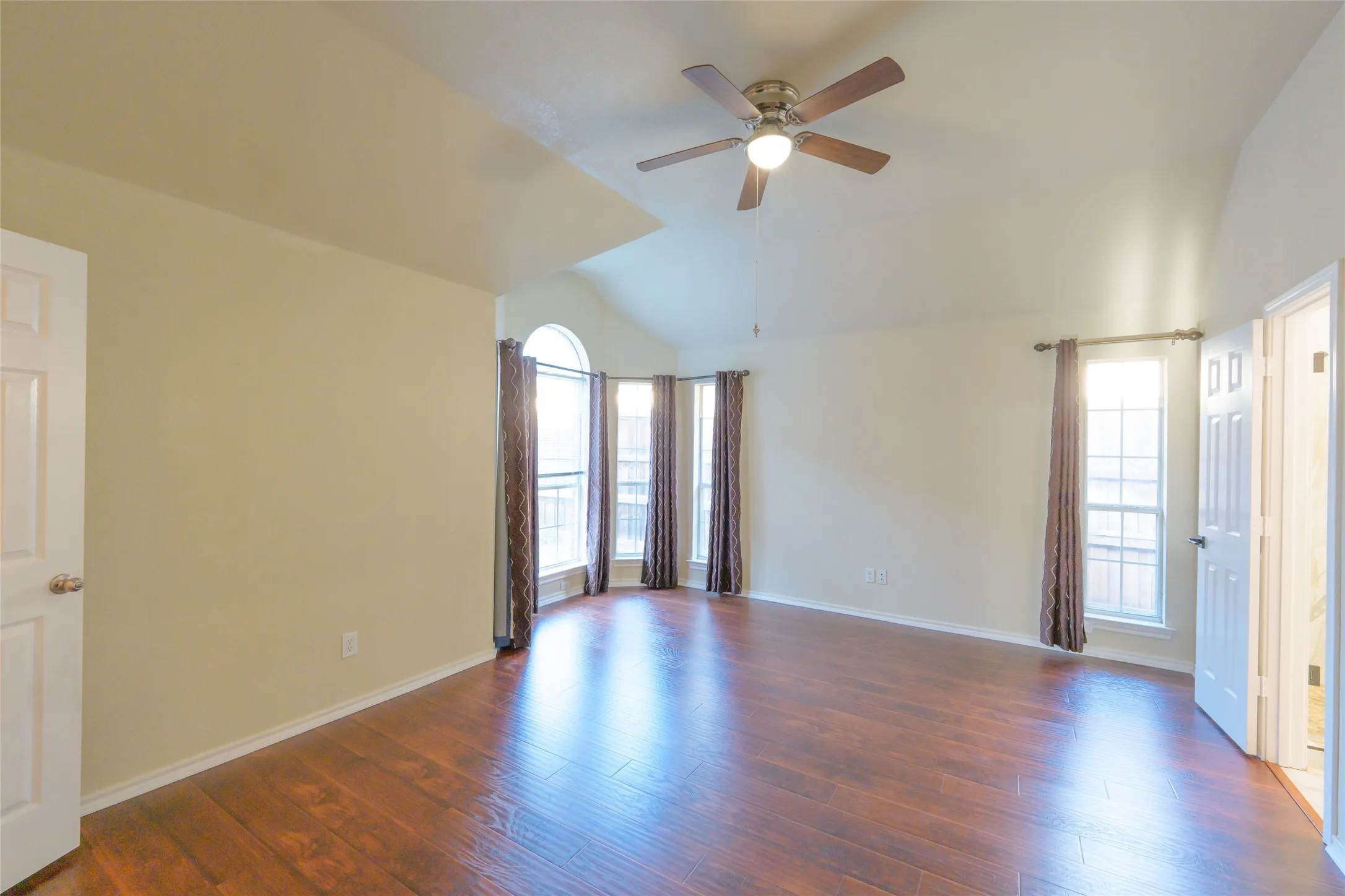 Vaulted ceiling with an integrated ceiling fan, wood-finish flooring, and multiple windows