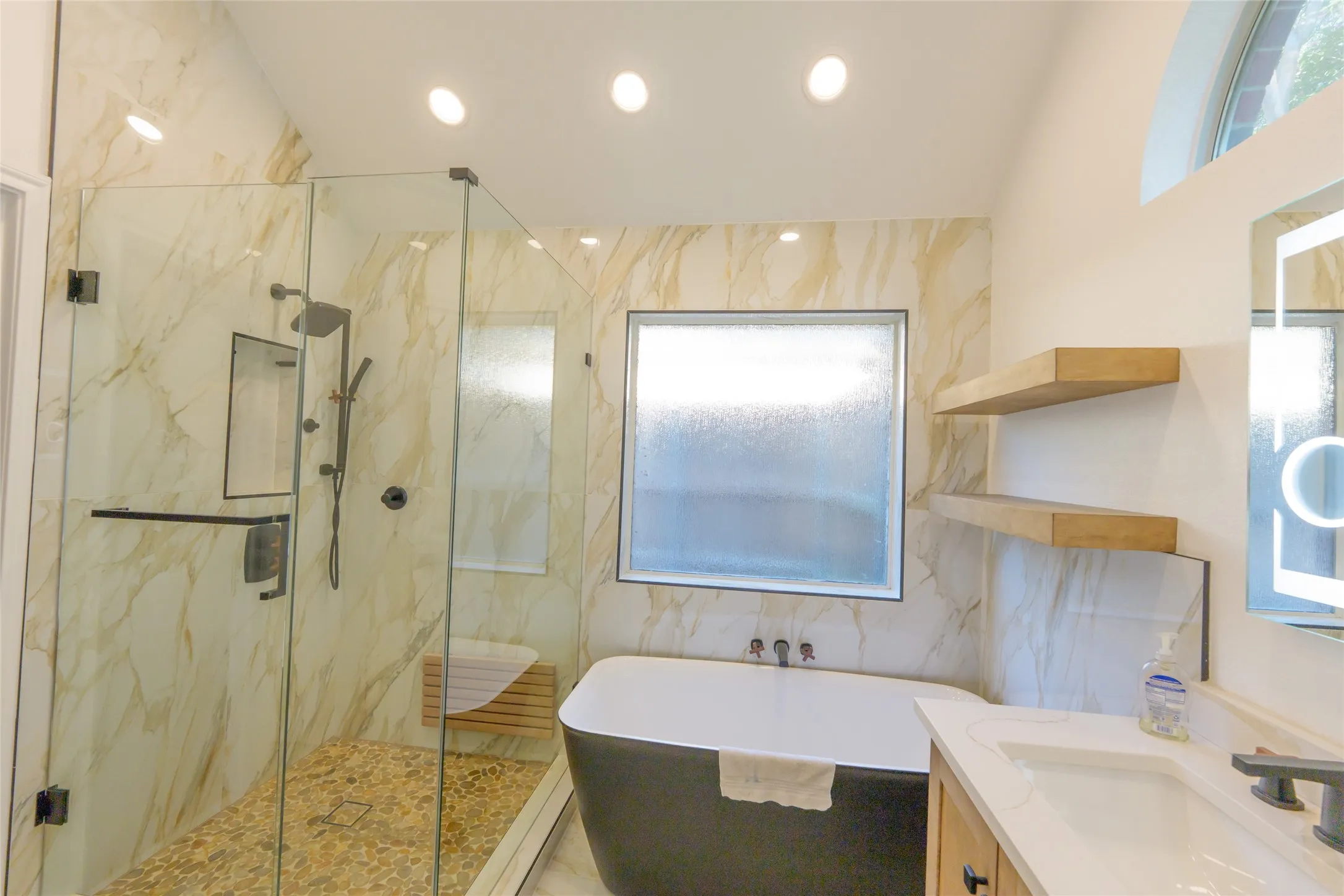 Glass-enclosed shower with pebble-tile flooring and wall-mounted shower system