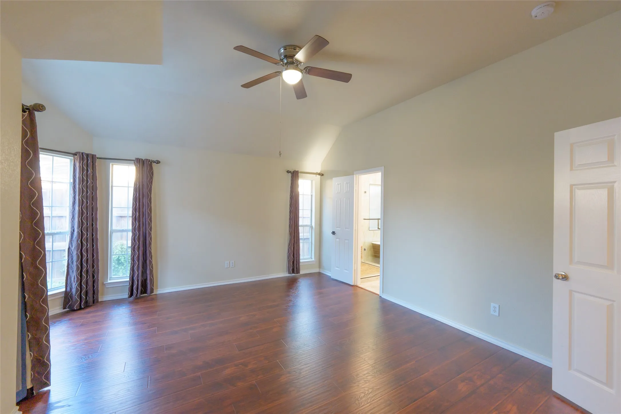 Vaulted ceiling, wood-finish flooring, ceiling fan with integrated lighting, multiple windows, and a panel door