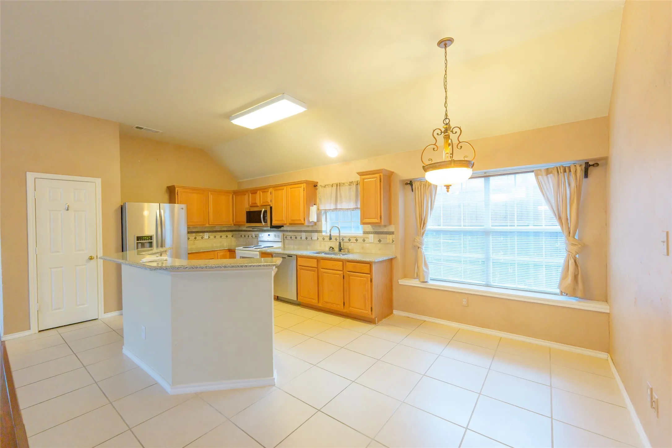 Kitchen featuring light wood-finish cabinetry, stainless steel appliances, a breakfast bar, and tile flooring