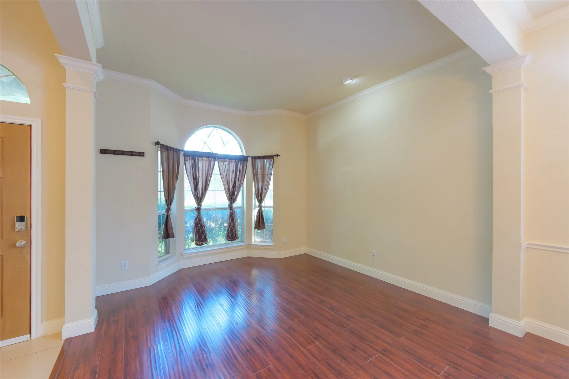 Wood-finish flooring, bay window with arched transom, recessed lighting, crown molding, and decorative columns