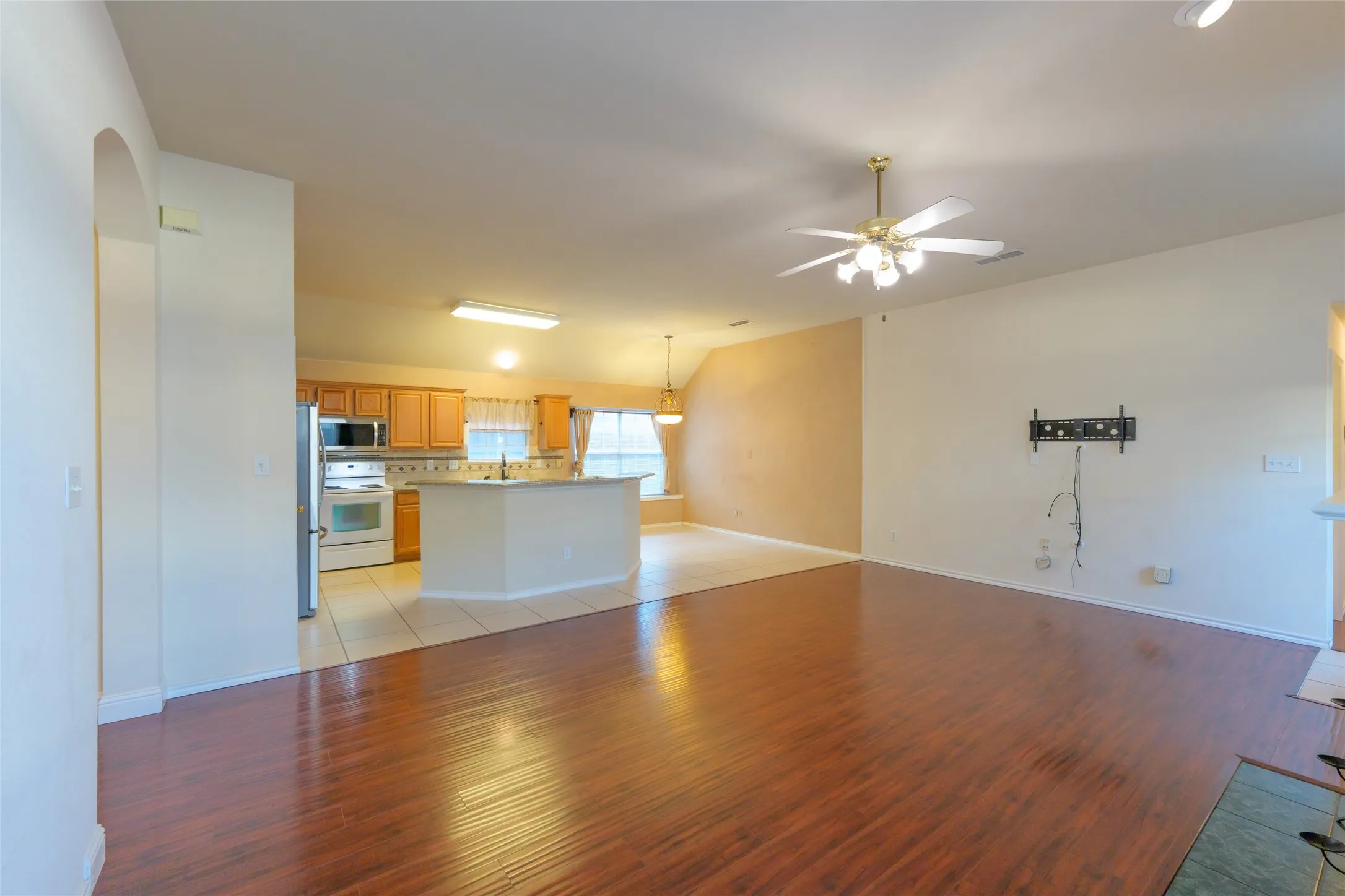Wood-finish flooring, ceiling fan with integrated lighting, kitchen island, stainless steel refrigerator, and white built-in oven