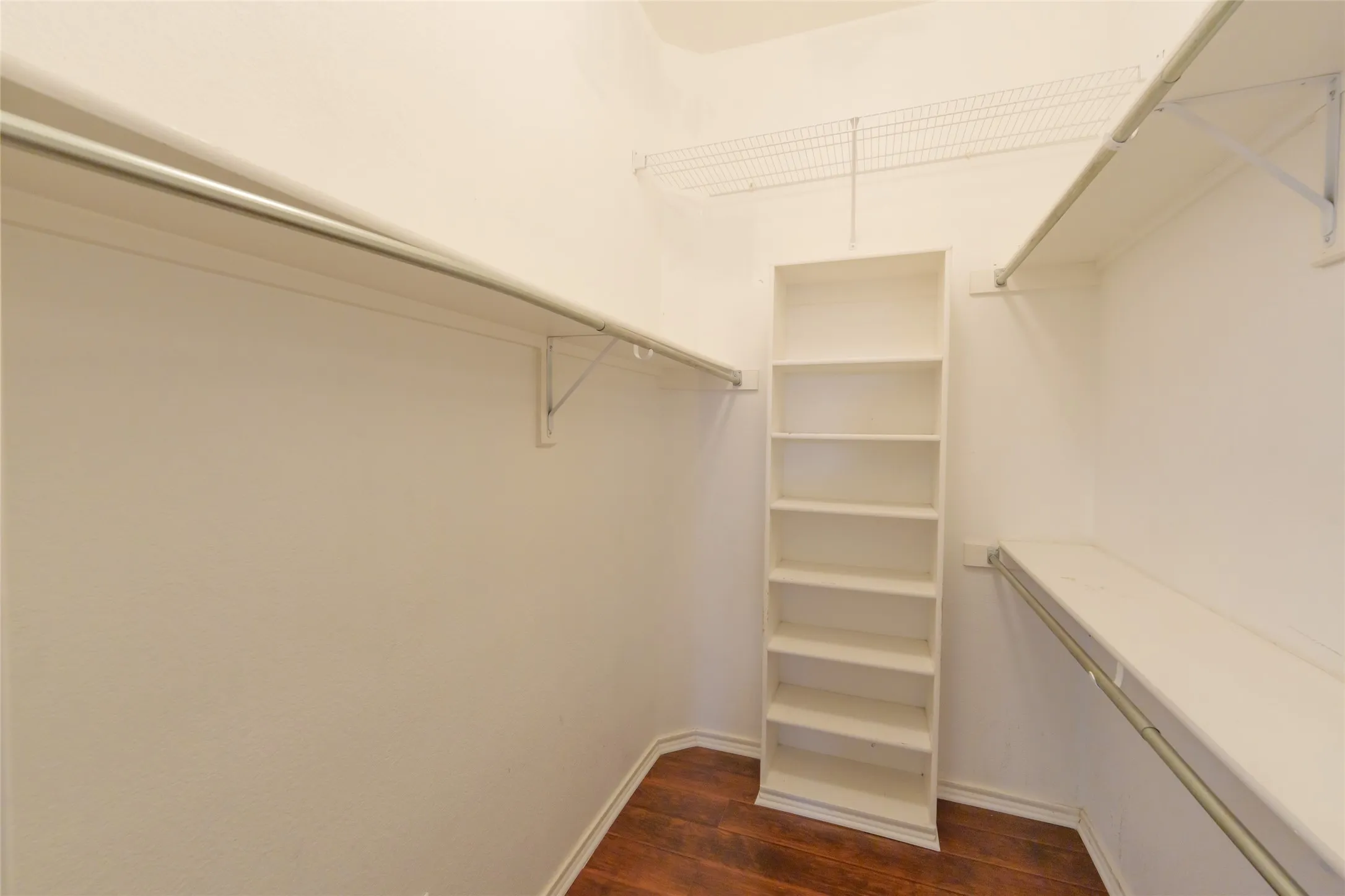 Walk-in closet with wood-finish flooring, built-in shelving, and multiple hanging rods