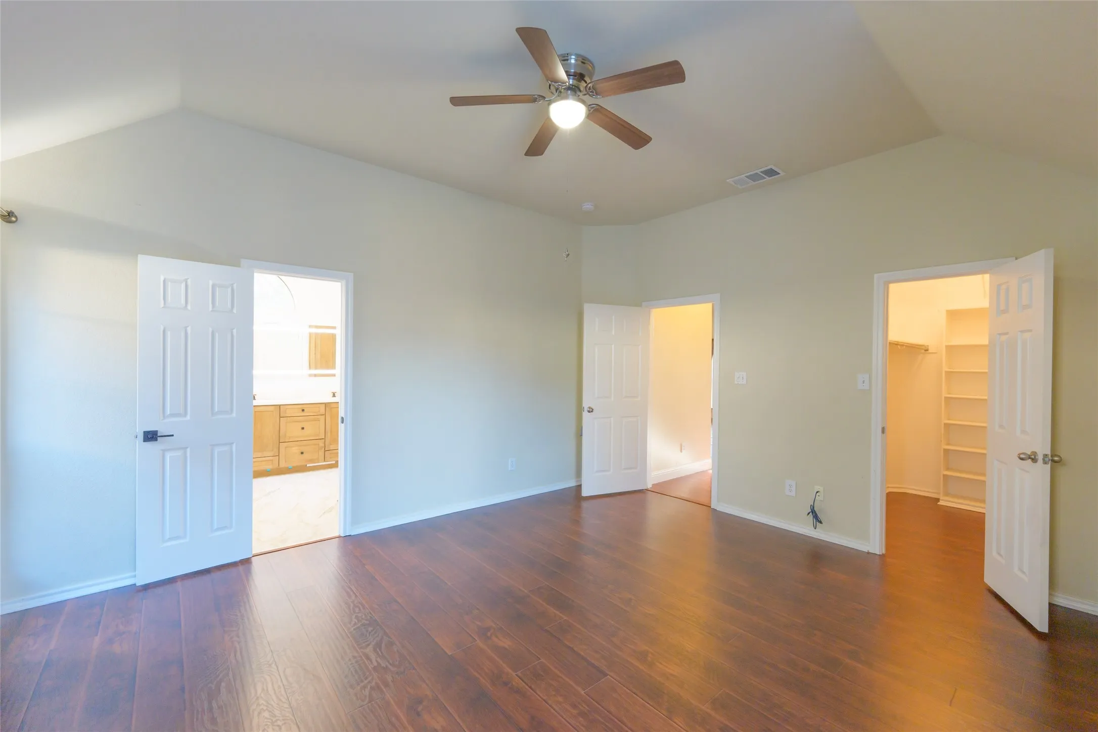 Vaulted ceiling, wood-finish flooring, ceiling fan with integrated lighting, built-in closet shelving, and a vanity with wood-finish cabinetry