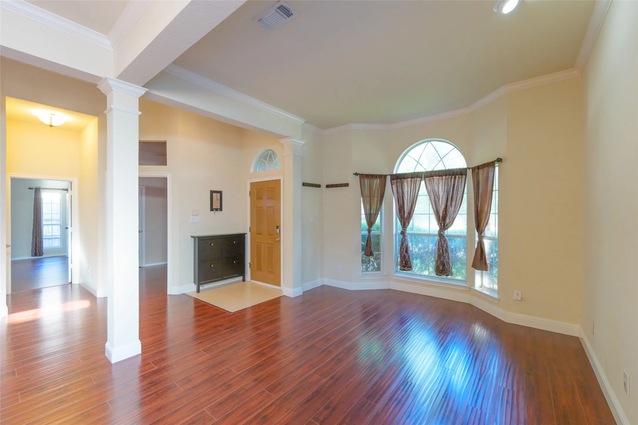 Wood-finish flooring throughout, decorative columns, arched transom window over the entry door, bay window configuration, and crown molding