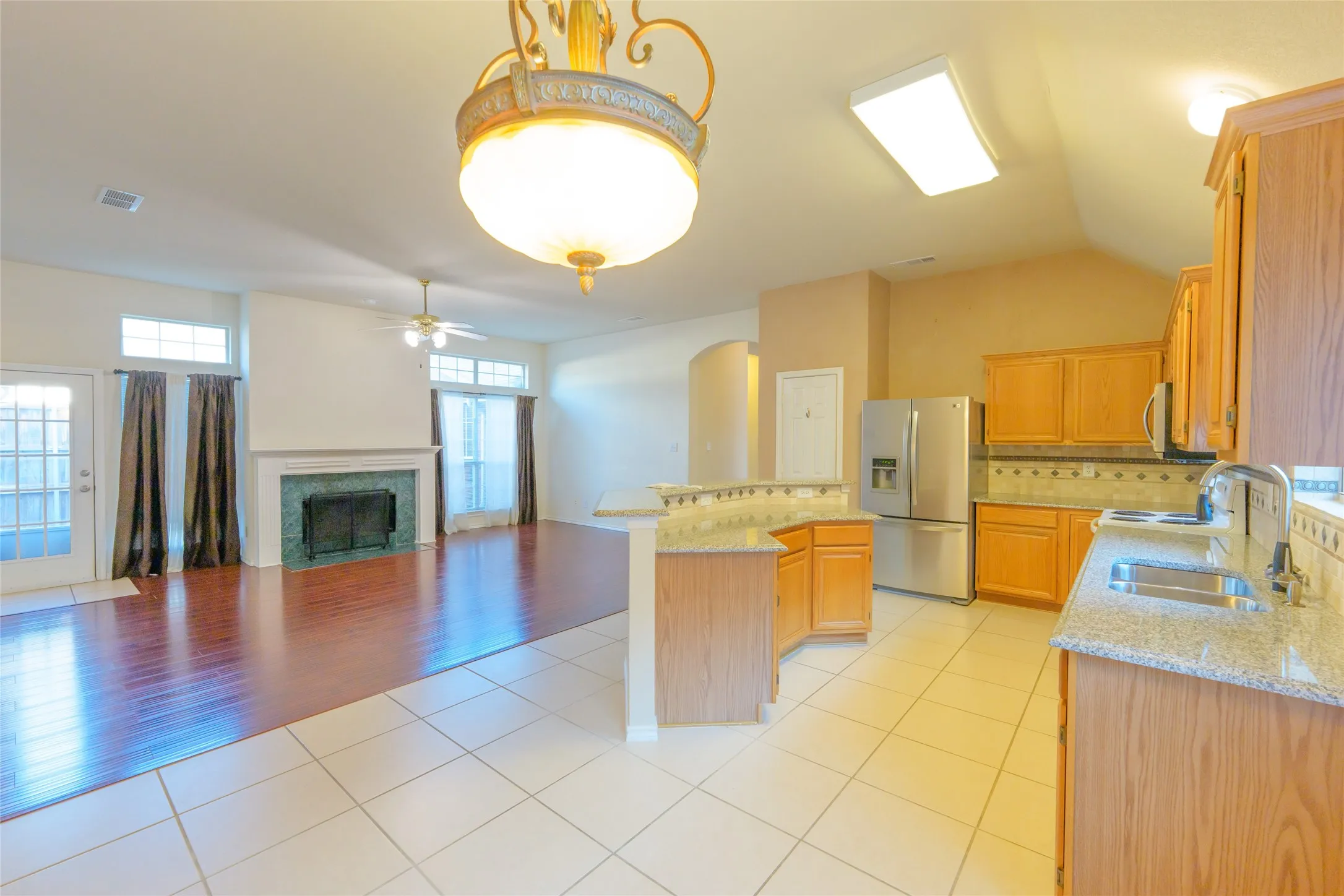 Open-concept design featuring a kitchen with light wood cabinetry, granite-finish countertops, and stainless steel appliances