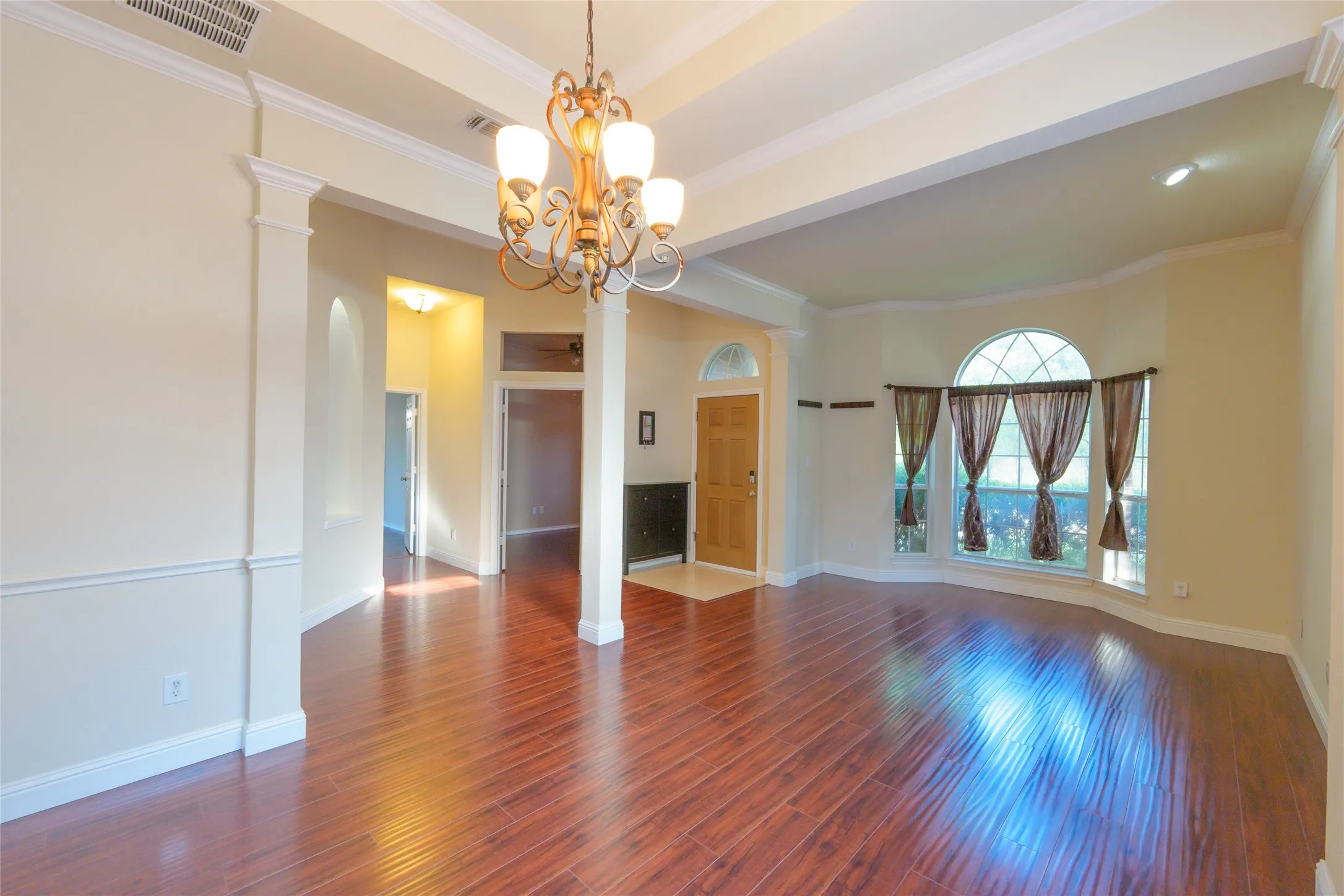 Wood-finish flooring, bay window with arched transom, decorative chandelier, crown molding, and wainscoting
