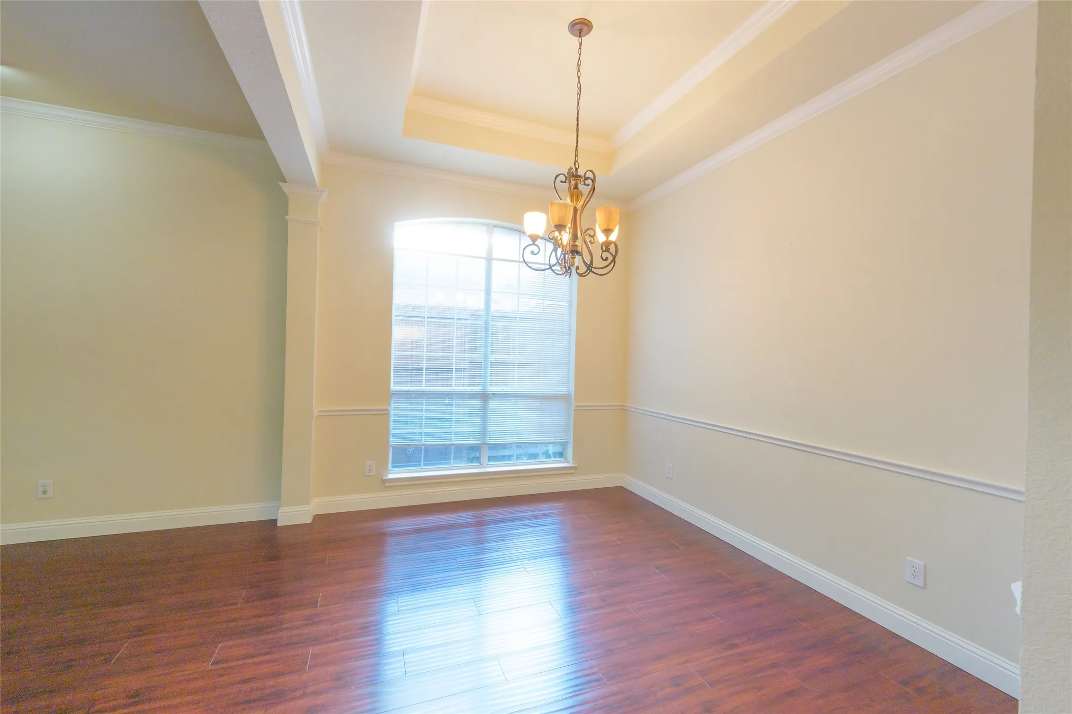 Wood-finish flooring, decorative ceiling trim, a rectangular window with grids, and a chandelier with amber glass shades
