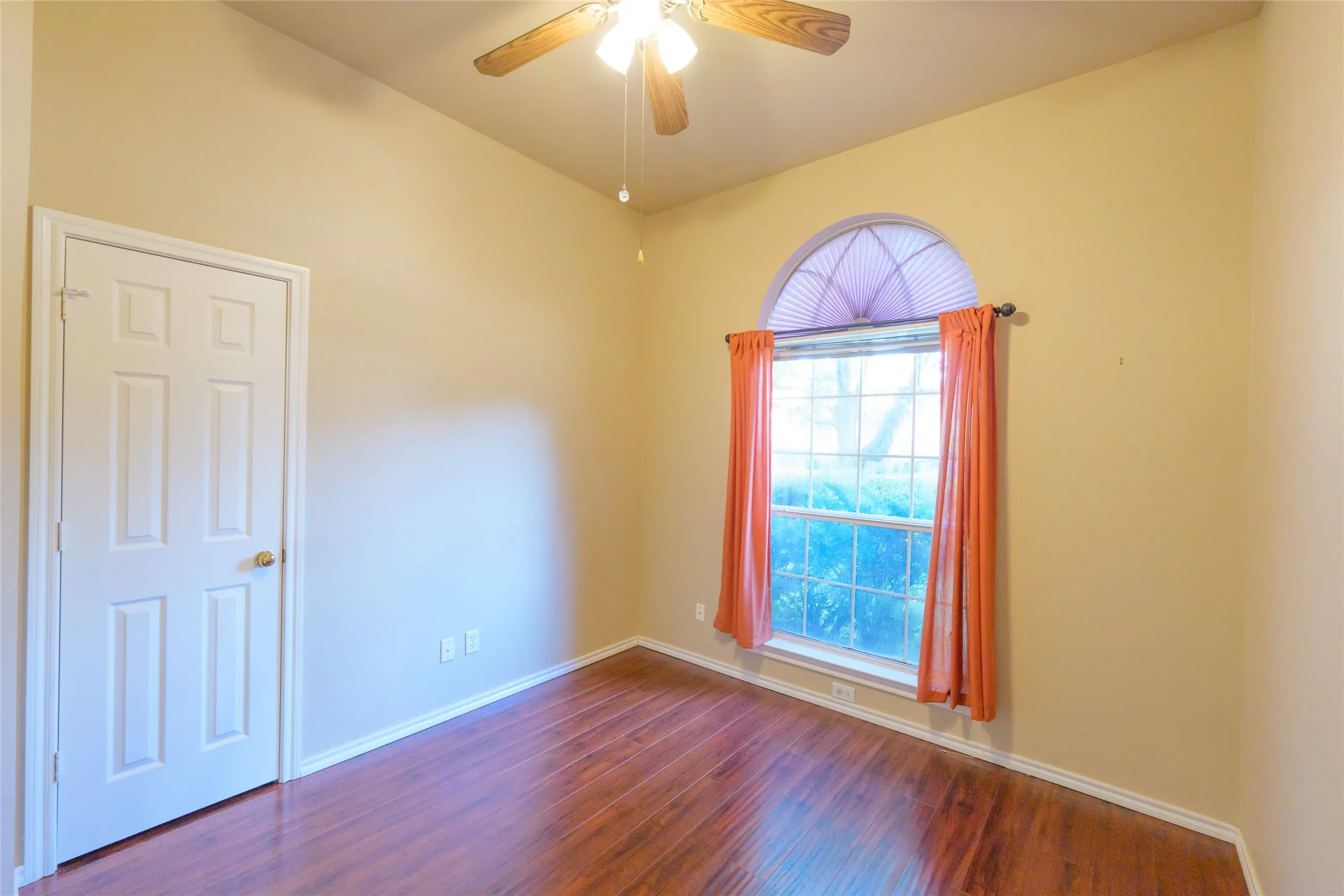 Arched window with window treatments, ceiling fan with light fixture, wood-finish flooring, and white trim