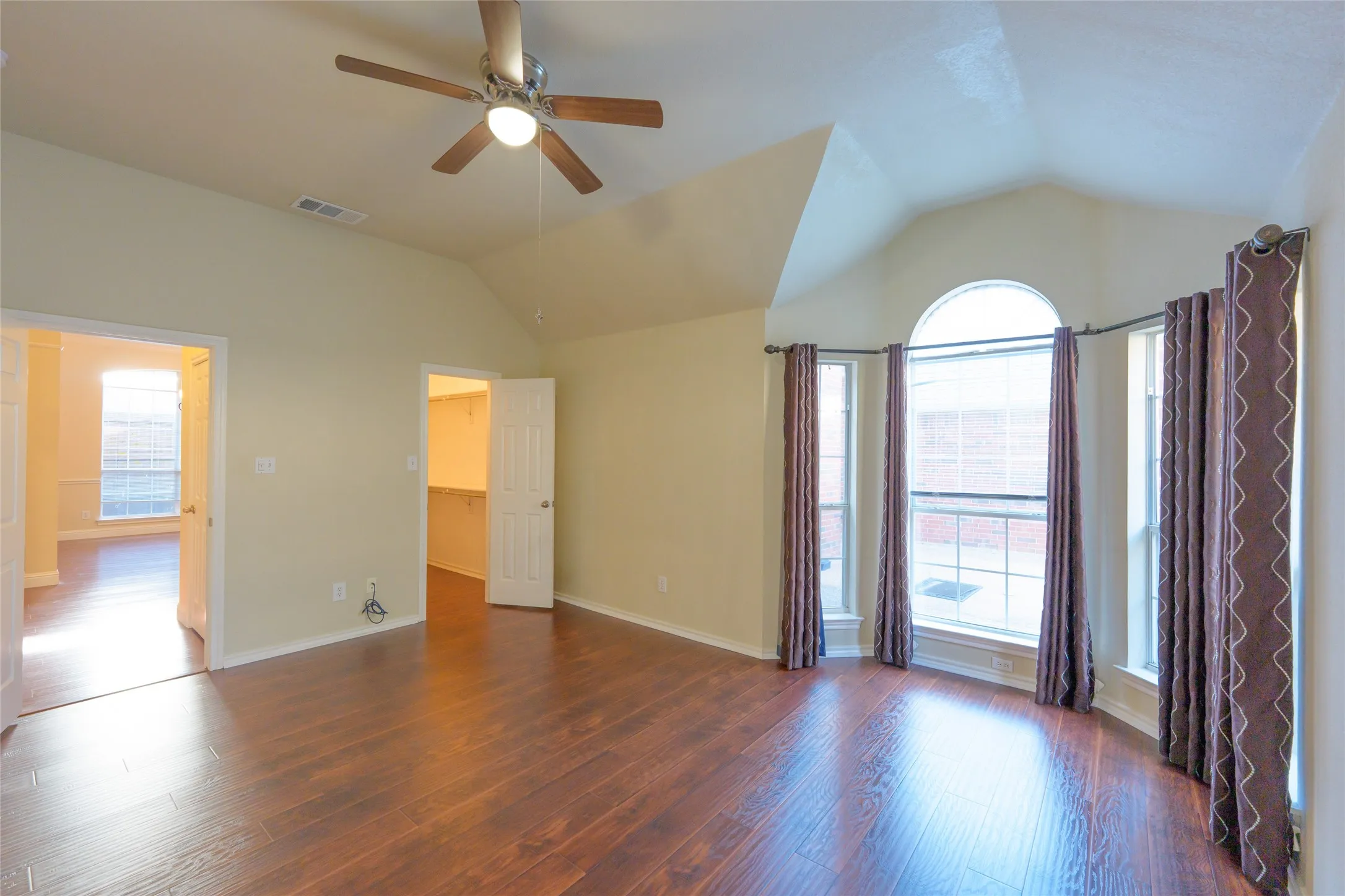 Wood-finish flooring, vaulted ceiling, ceiling fan, and a curved bay window with an arched transom