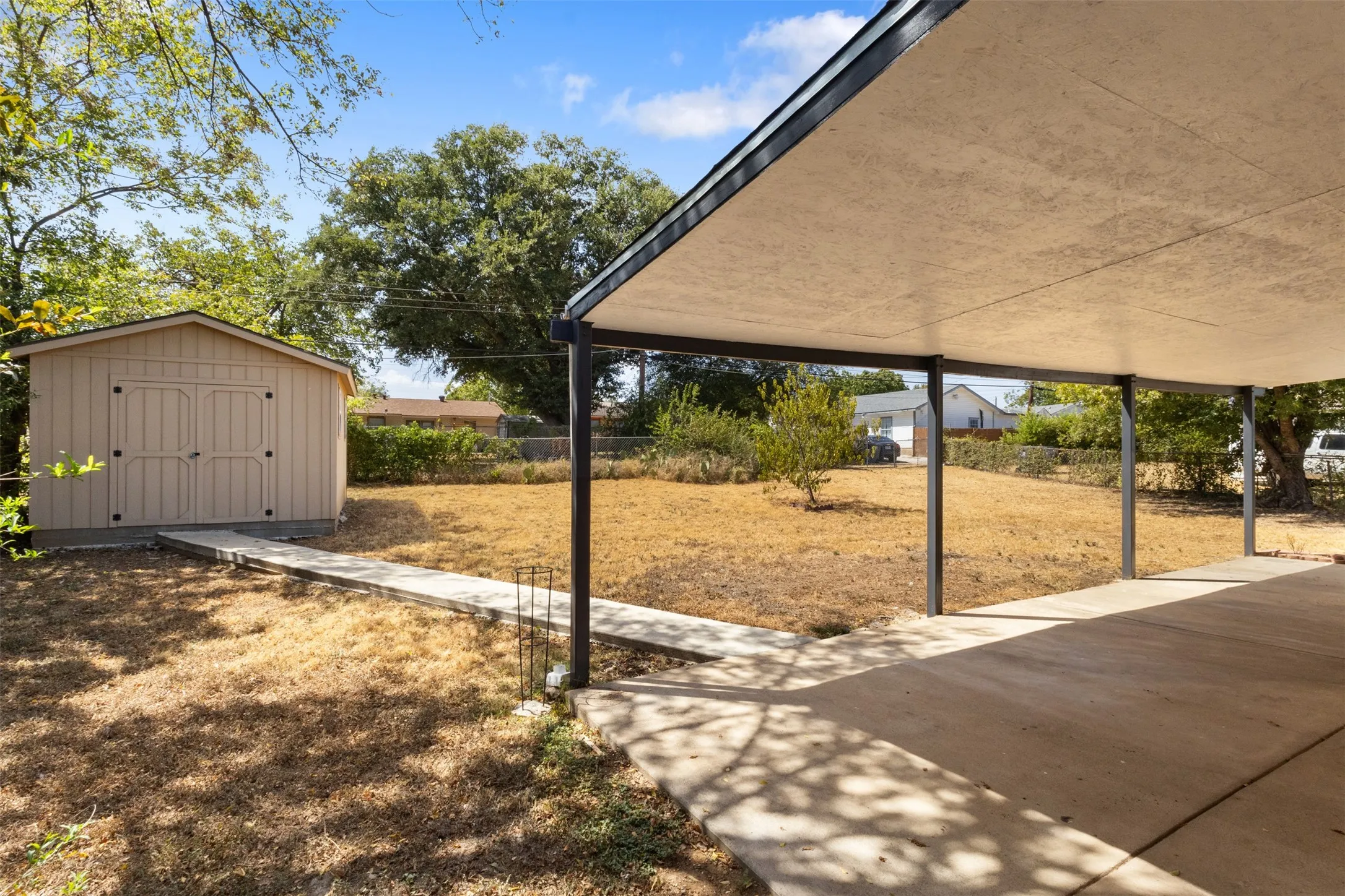 Expansive backyard featuring a covered patio, concrete walkway, and a detached storage shed