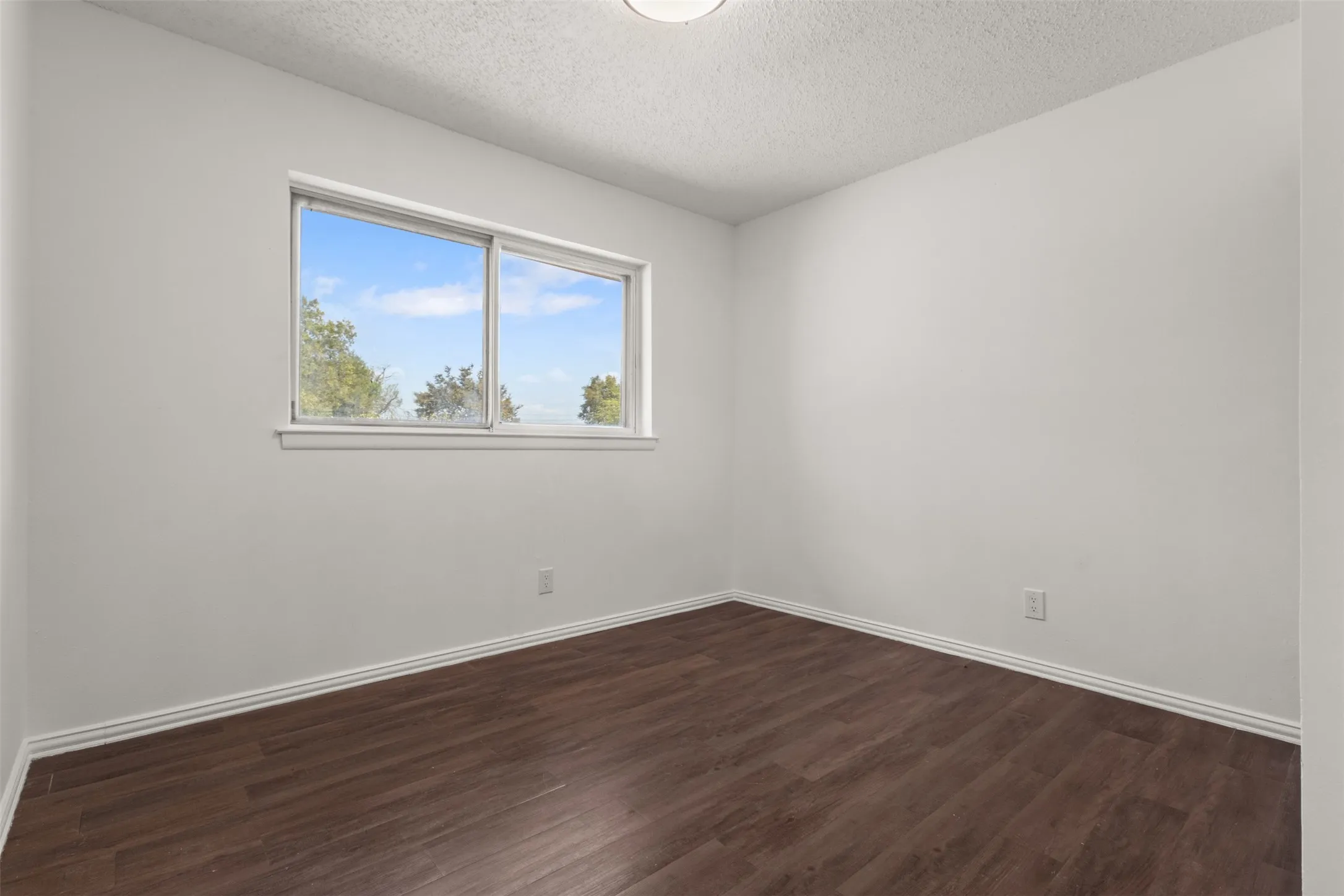 Interior room featuring a large window, dark wood-finish flooring, and white walls