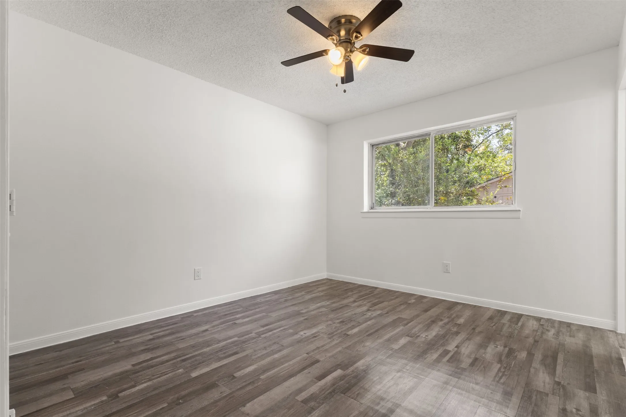 Wood-finish flooring, white walls, window, and ceiling fan with integrated lighting