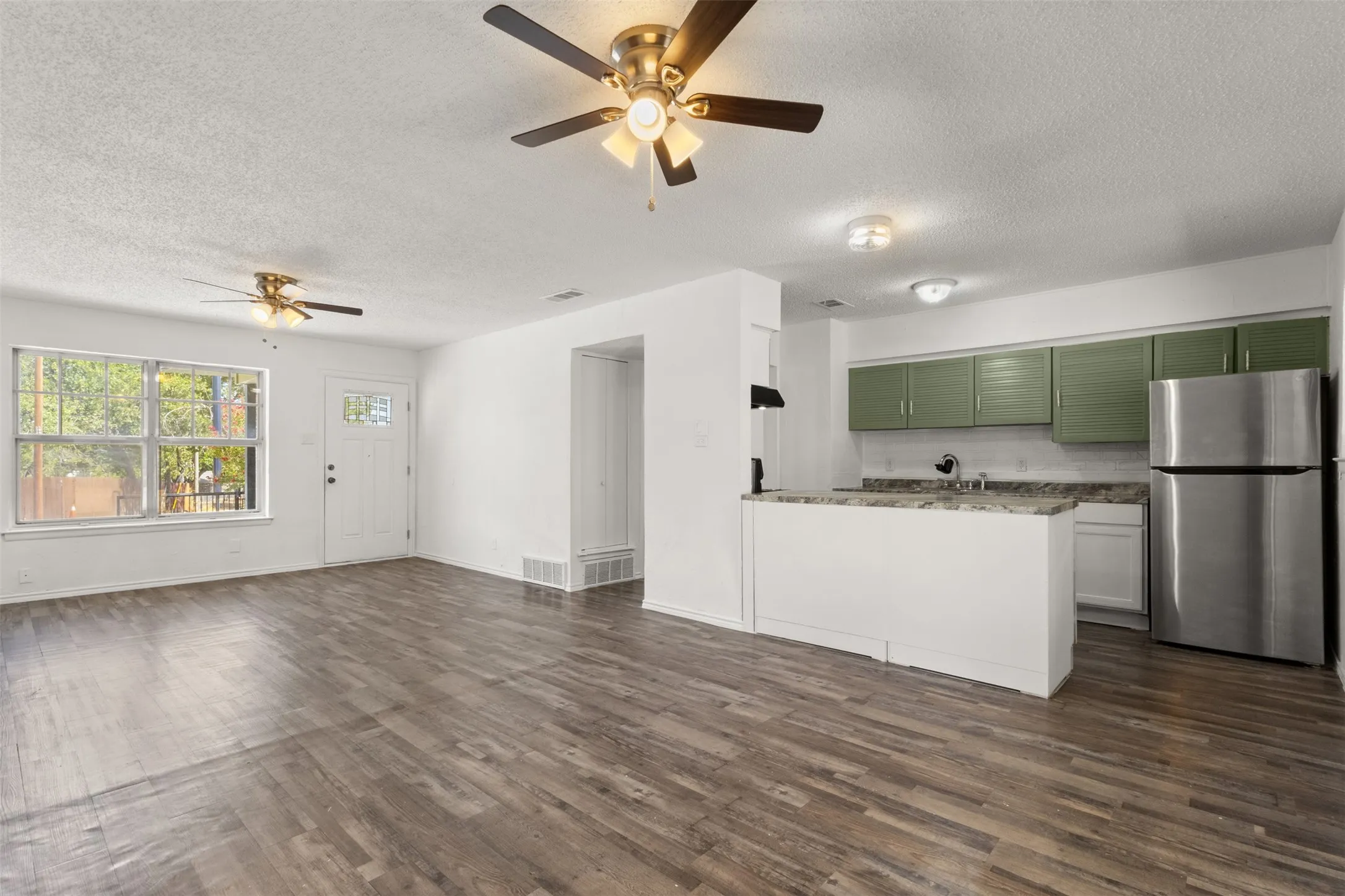Open-concept living space featuring wood-finish flooring, white walls, and dual ceiling fans