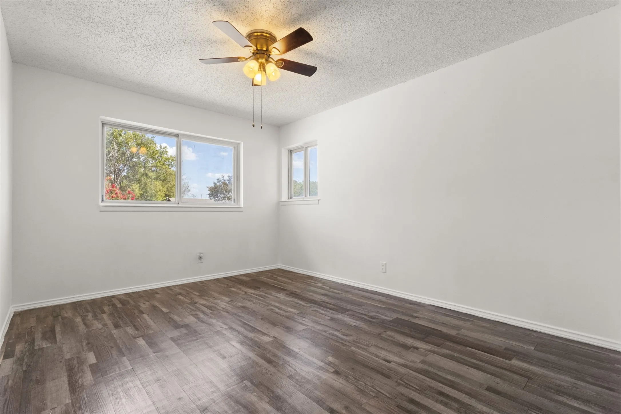 Wood-finish flooring, white painted walls, ceiling fan with integrated lighting, and multiple windows