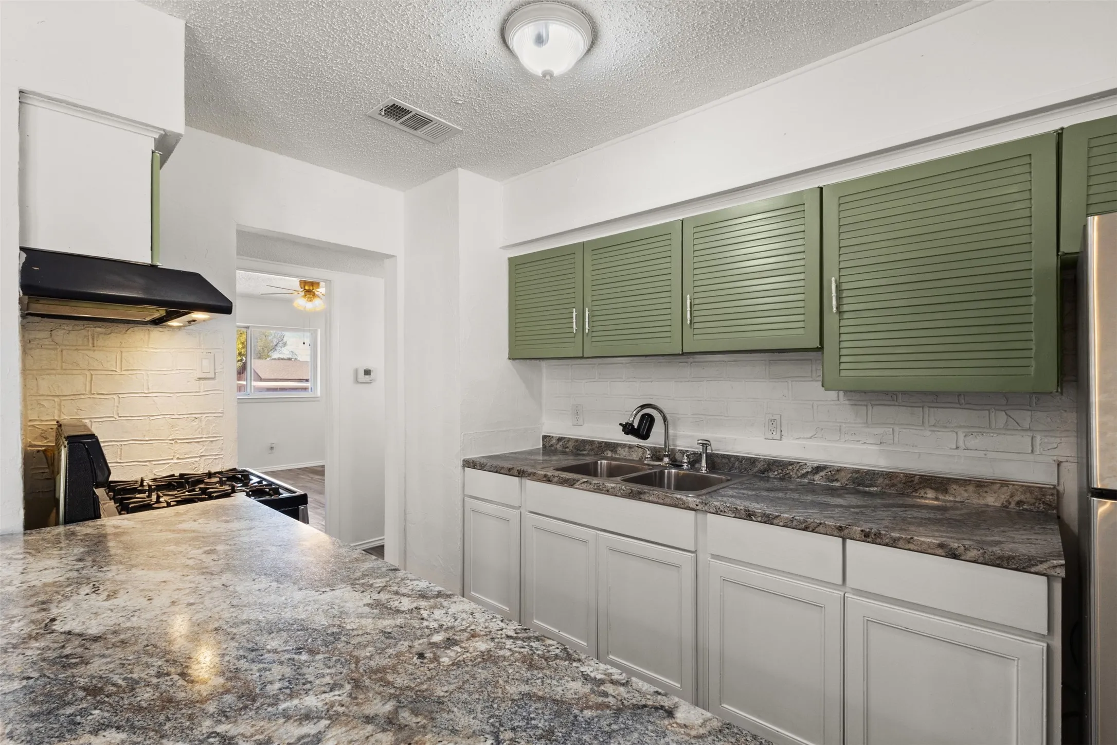 Kitchen featuring light green upper cabinetry, white lower cabinetry, and a double basin stainless steel sink