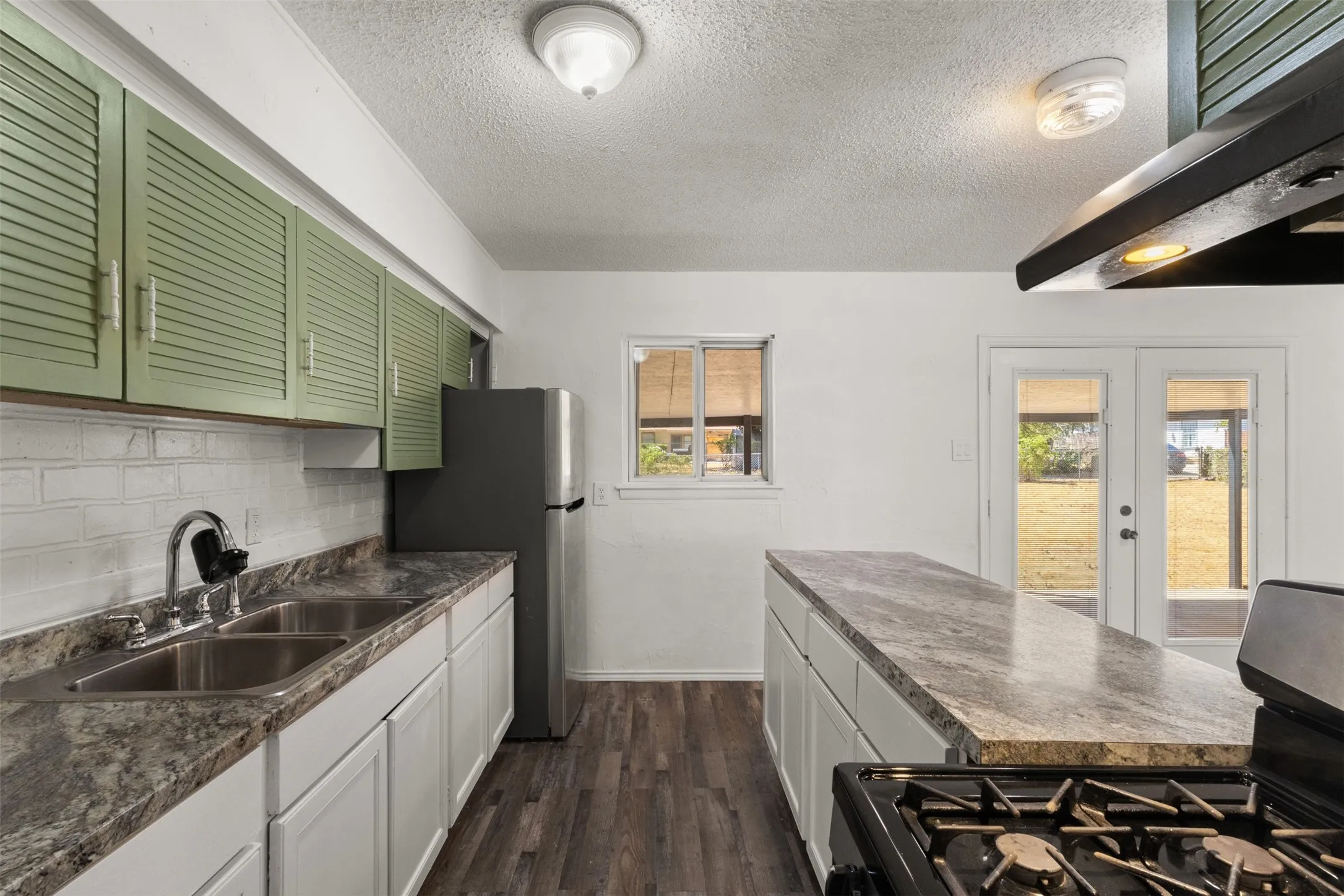 Kitchen featuring a dual basin sink, white cabinetry, wood-finish flooring, a center island with a countertop, and double glass doors leading to the exterior