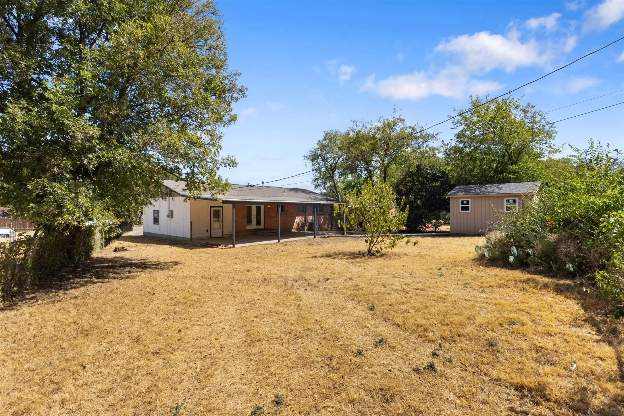 Expansive backyard featuring a covered patio, a detached storage shed with windows, and mature trees