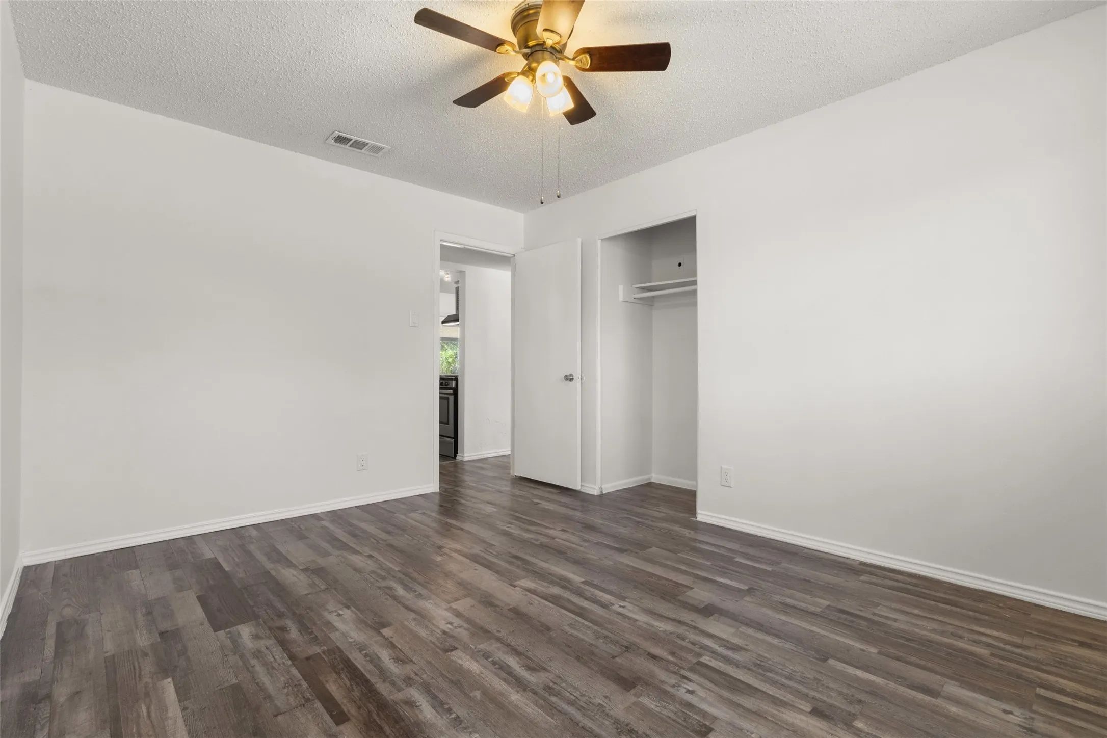 Wood-finish flooring, ceiling fan with integrated lighting, recessed clothing rod, and white walls
