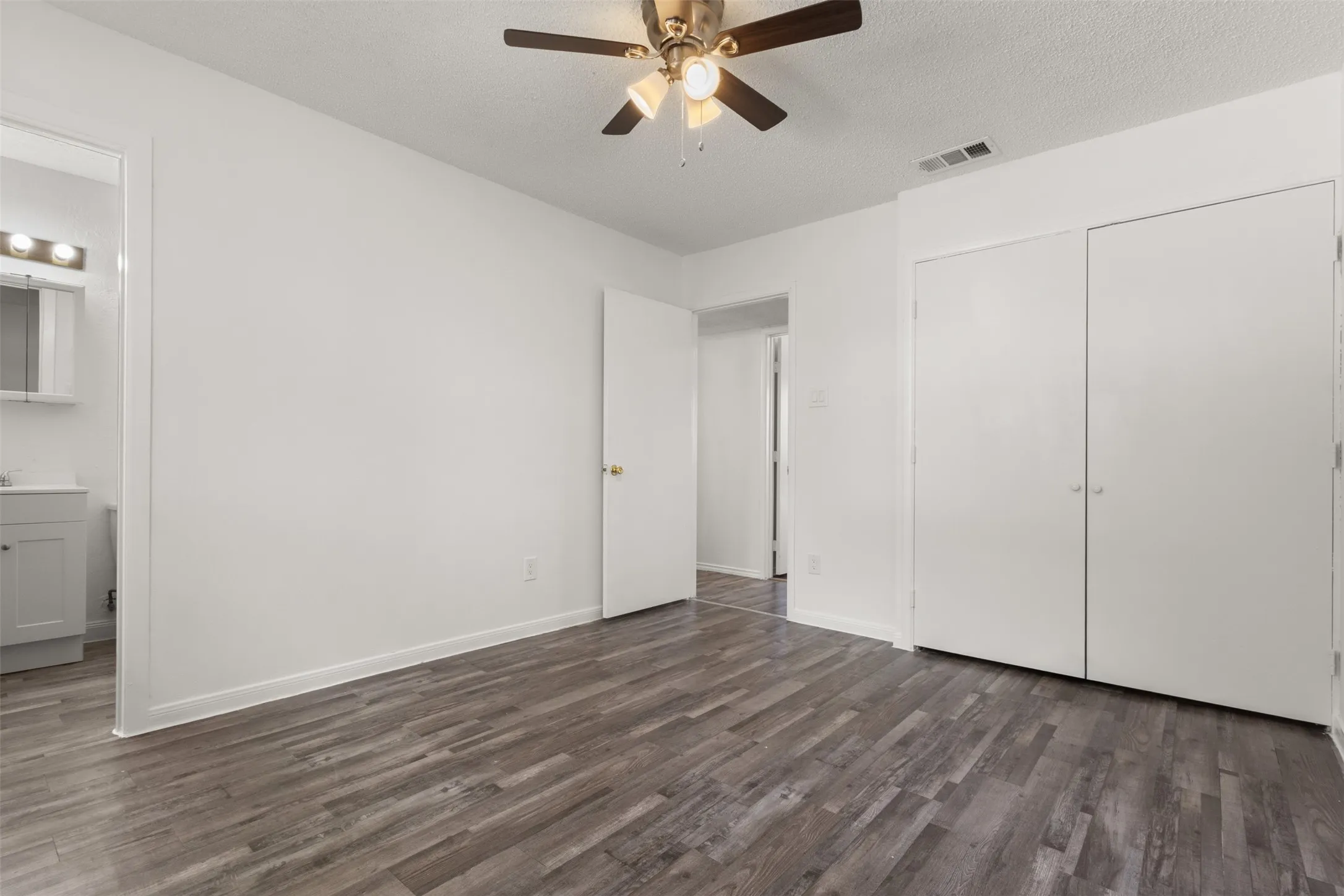 Wood-finish flooring, ceiling fan with light fixture, built-in closet with double doors, and a vanity with a mirror and light bar