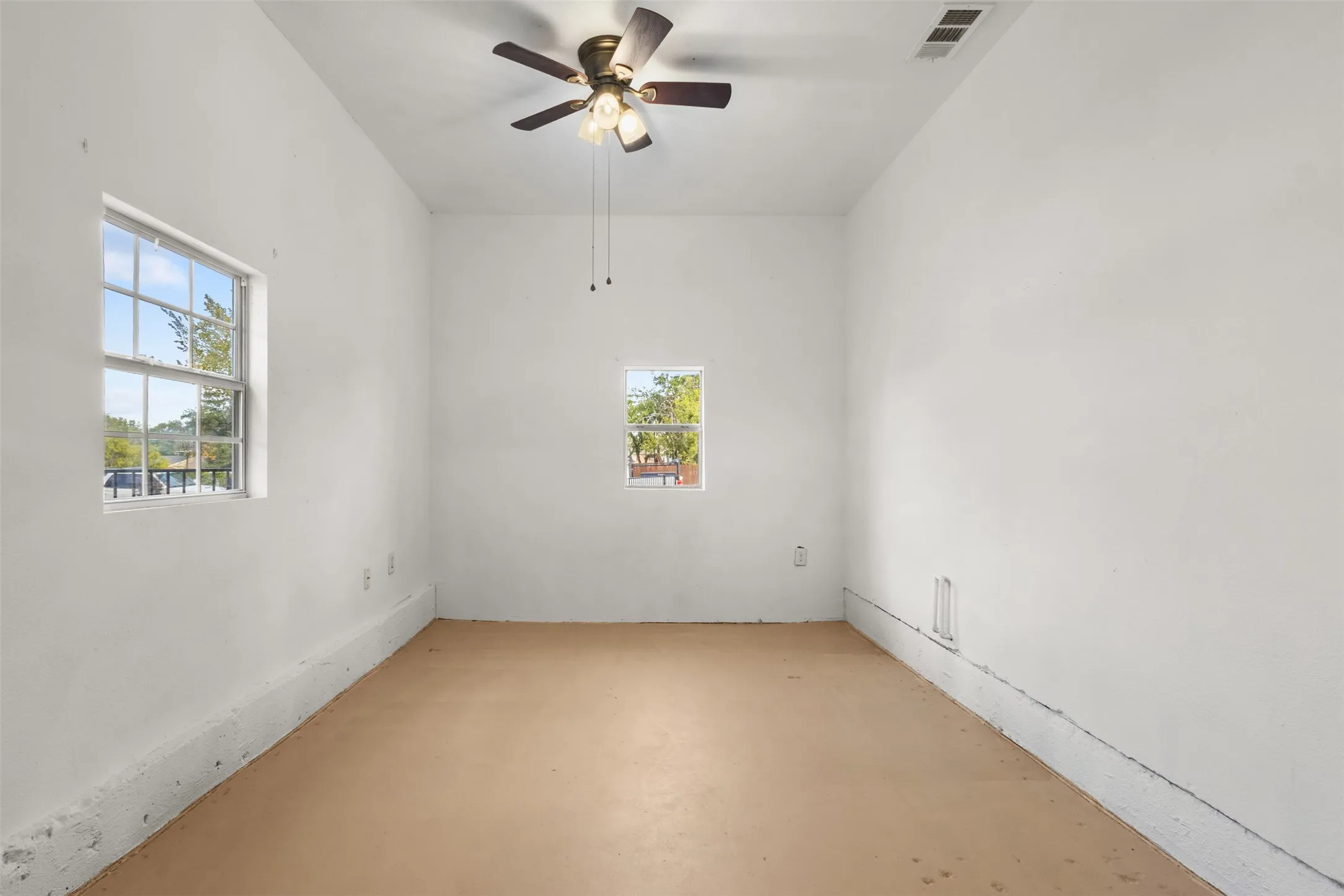 White painted walls, two windows providing natural light, ceiling fan with integrated lighting, and a neutral-toned floor