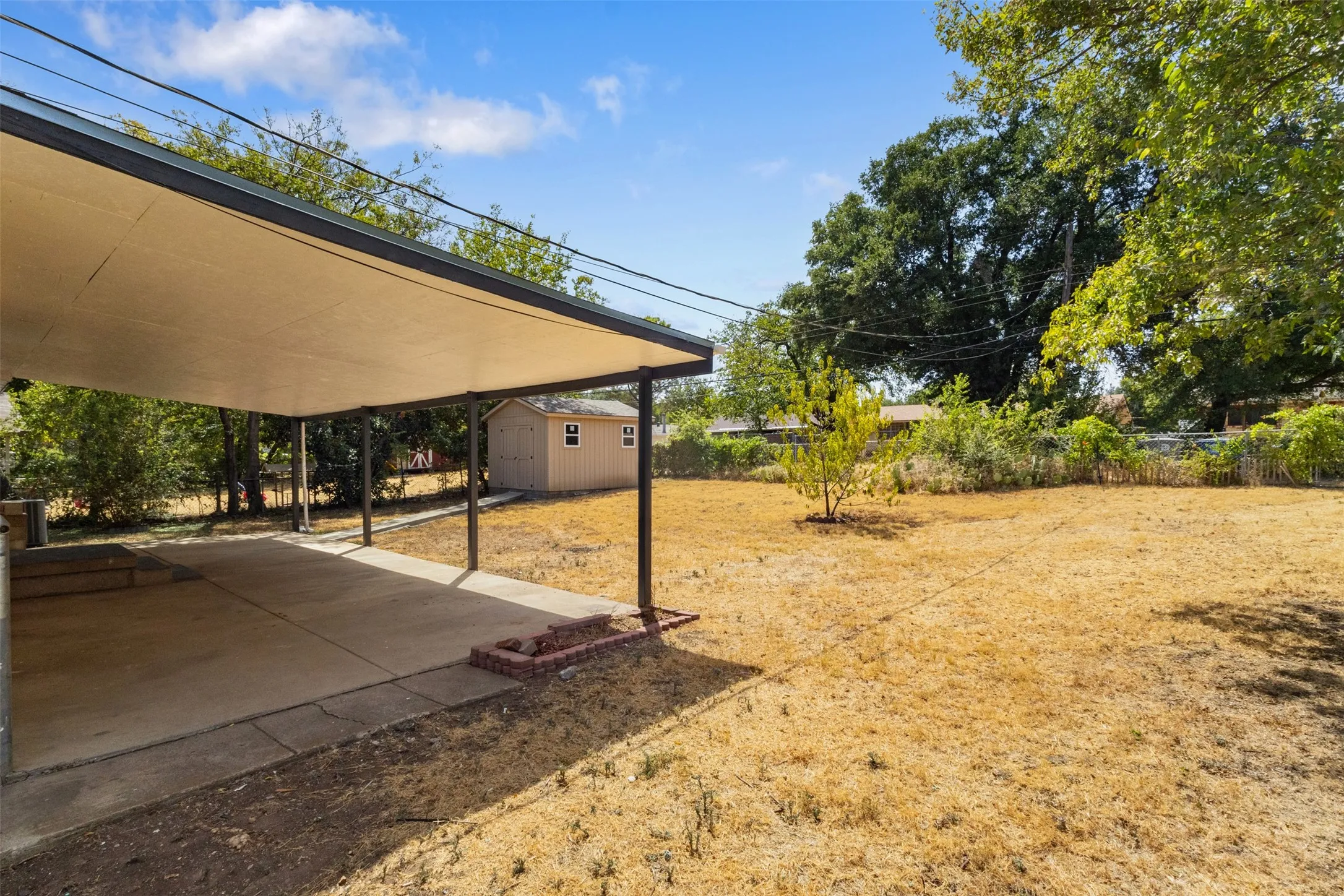 Covered concrete patio with metal support posts, complemented by a detached storage shed