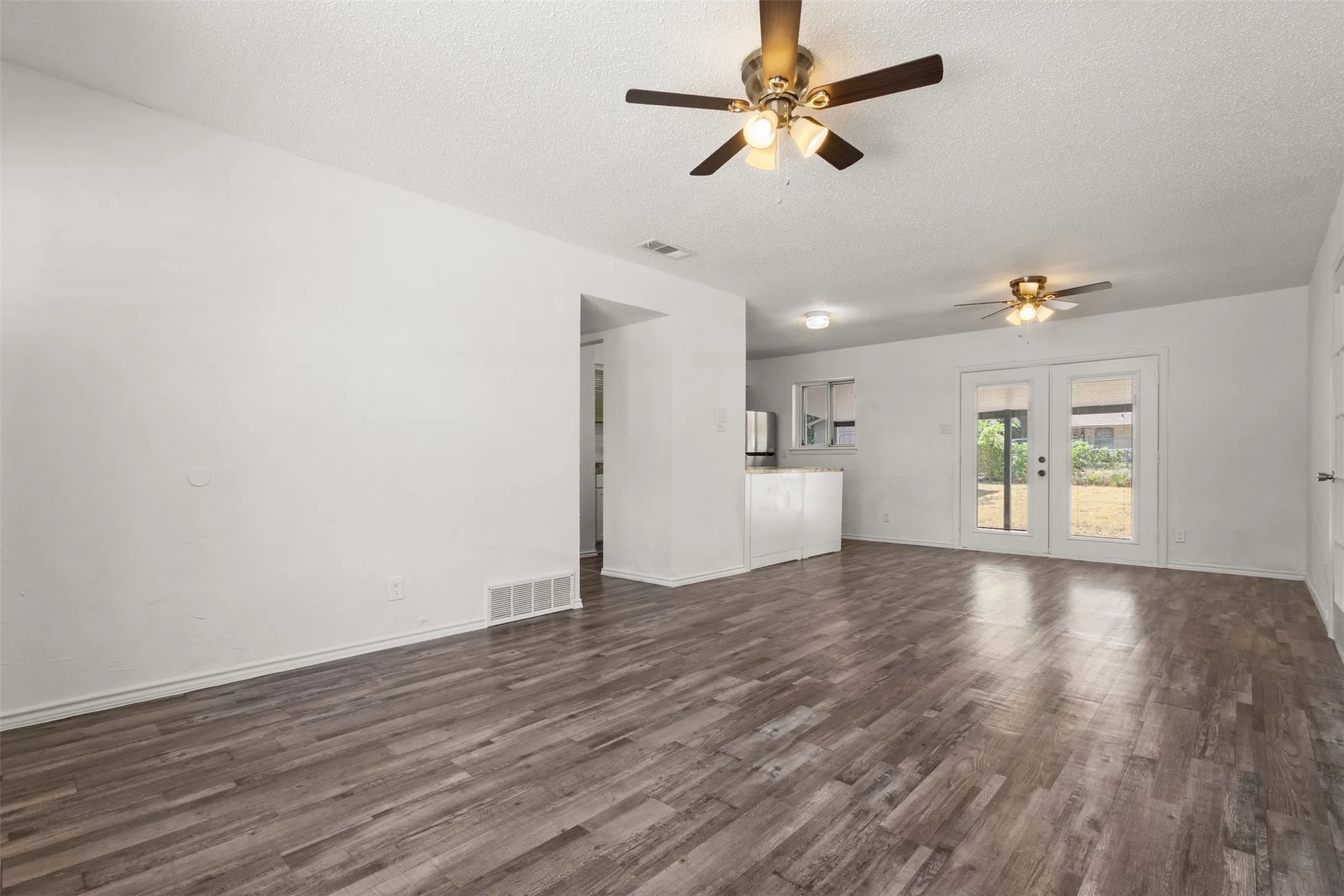 Spacious living area featuring wood-finish flooring, two ceiling fans, and double French doors providing access to the exterior