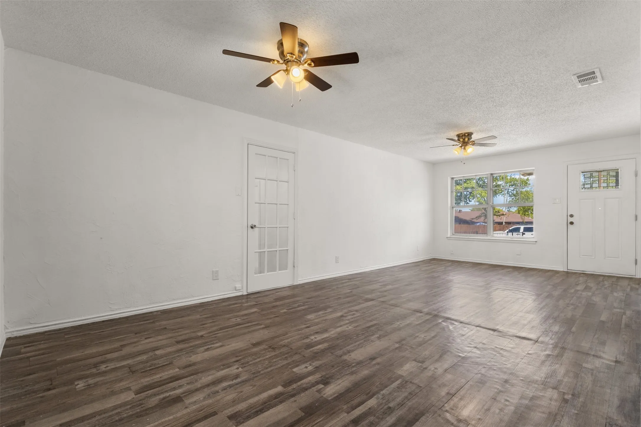 Wood-finish flooring, white painted walls, ceiling fans with integrated lighting, and a white paneled door with glass inserts