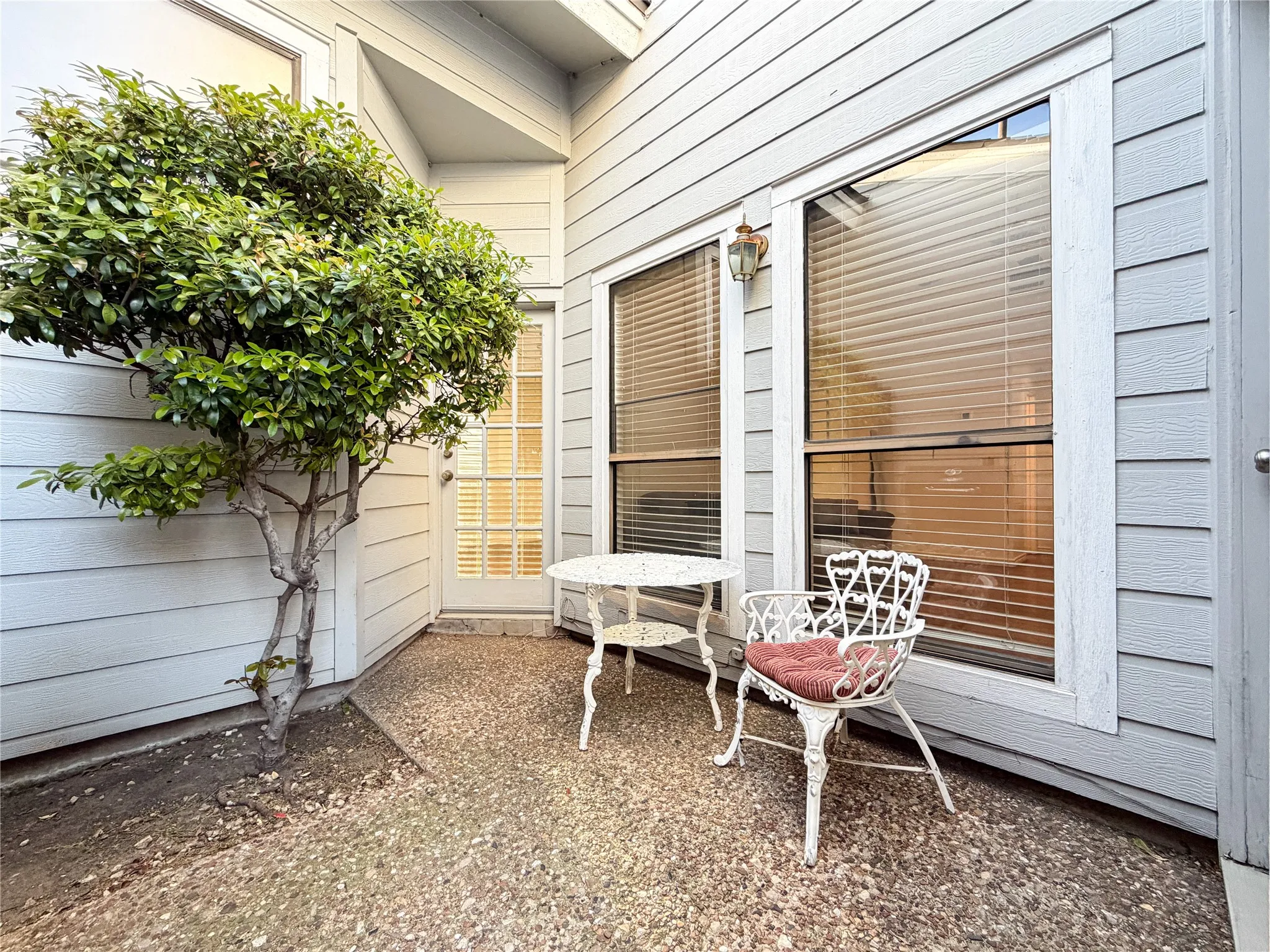 Pebble-finish patio with exterior siding, a decorative wall-mounted light fixture, and a glass-paneled door