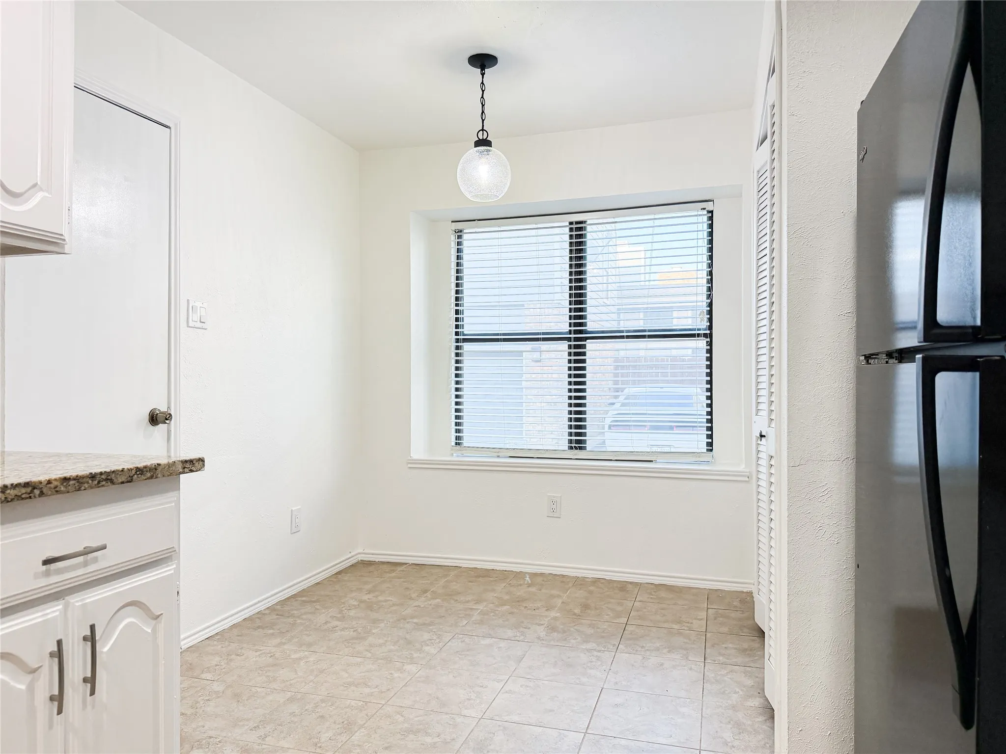 Recessed window with blinds, overhead pendant light, tile flooring, and white cabinetry with dark hardware