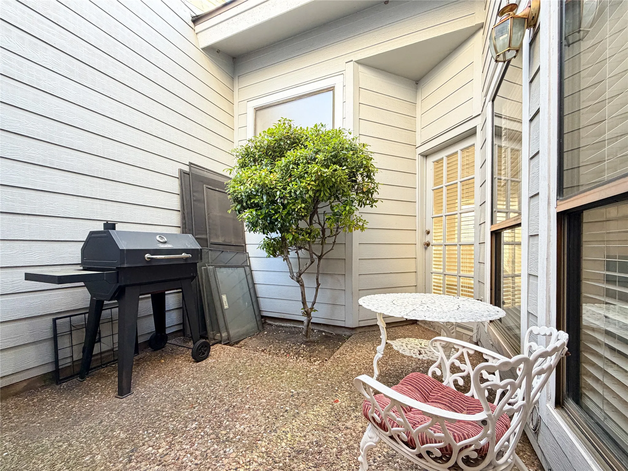 Enclosed gravel courtyard featuring a mature shrub and wood-finish siding