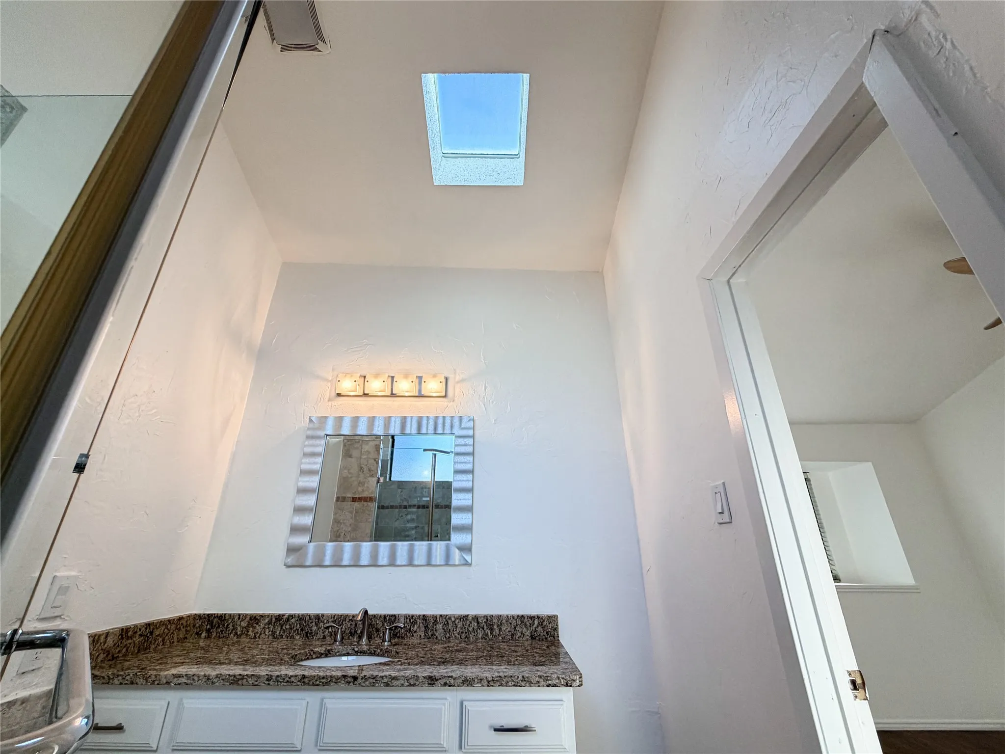 Vanity with a granite-style countertop, white cabinetry, and an undermount sink