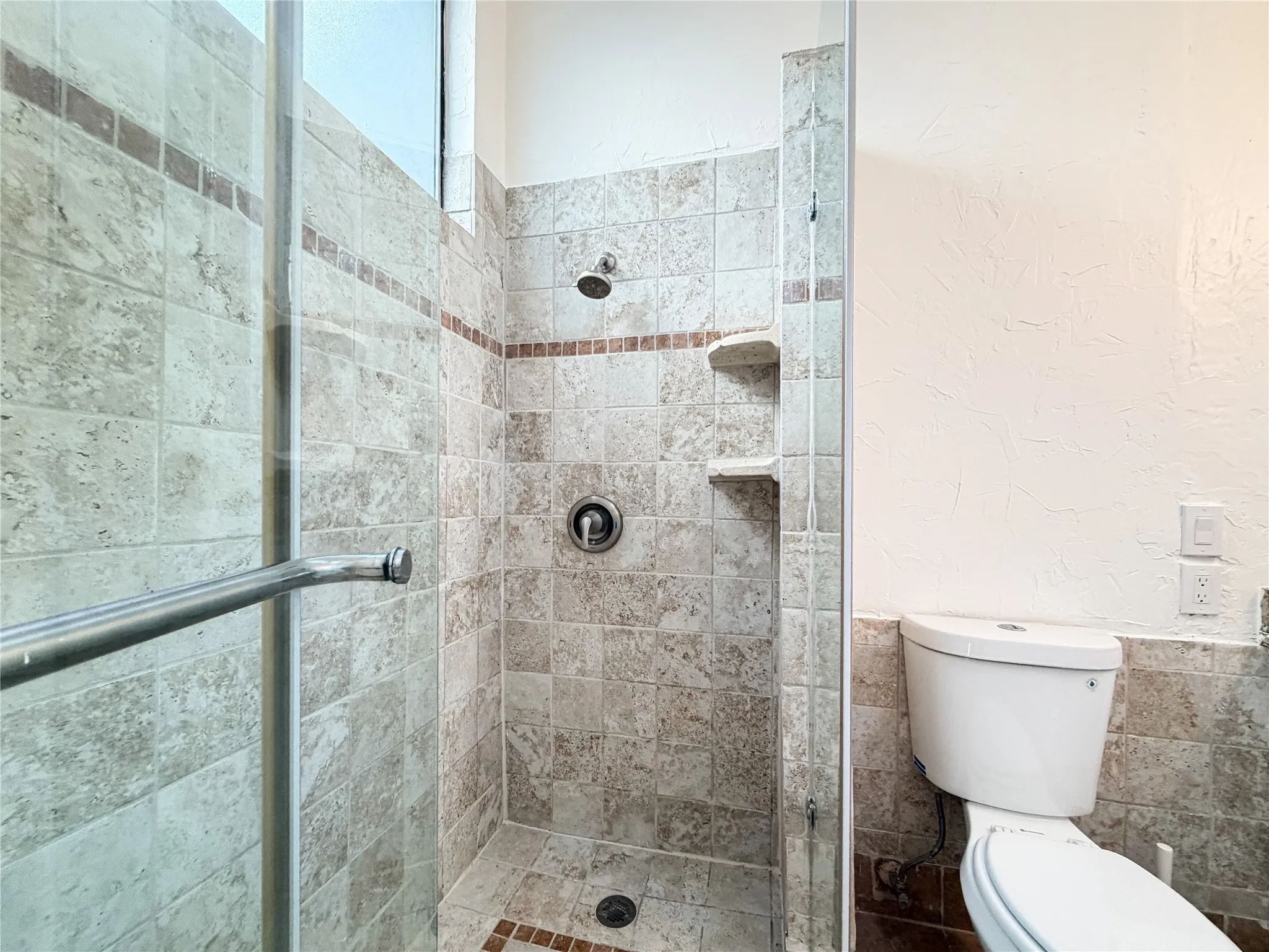 Glass-enclosed shower with tiled walls, integrated shelving, and a rain shower head