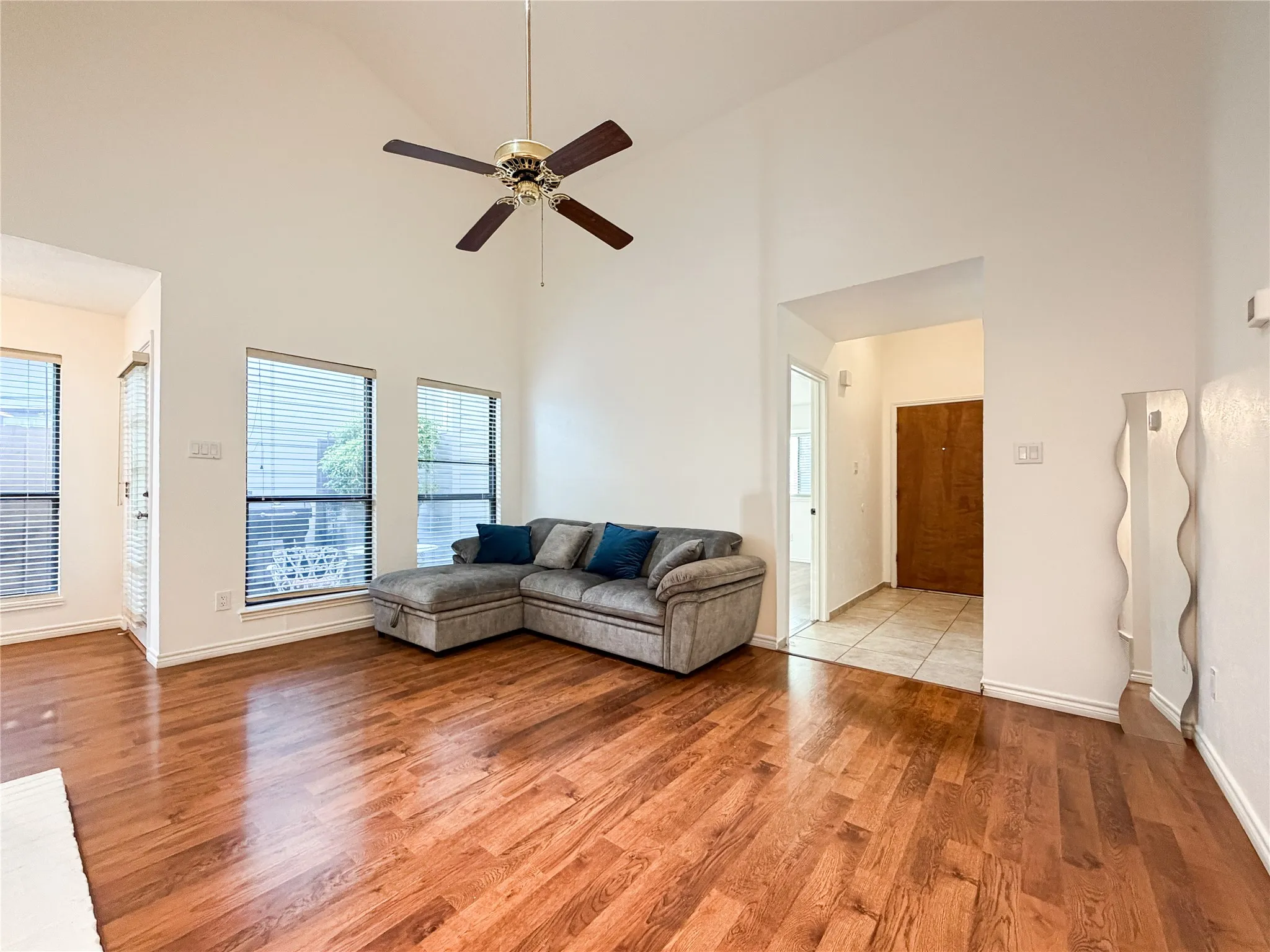 Hardwood-finish flooring, vaulted ceiling, ceiling fan, multiple windows with blinds, and a tiled entryway