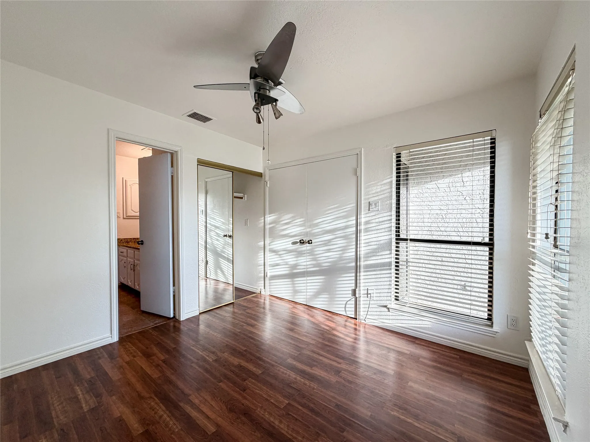 Wood-finish flooring, ceiling fan, white paneled walls, two-pane window, and a mirrored closet door