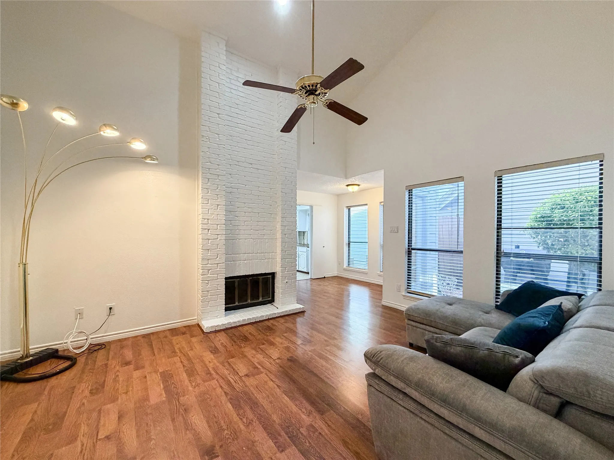 Vaulted ceiling with a ceiling fan, white brick fireplace, wood-finish flooring, and multiple windows