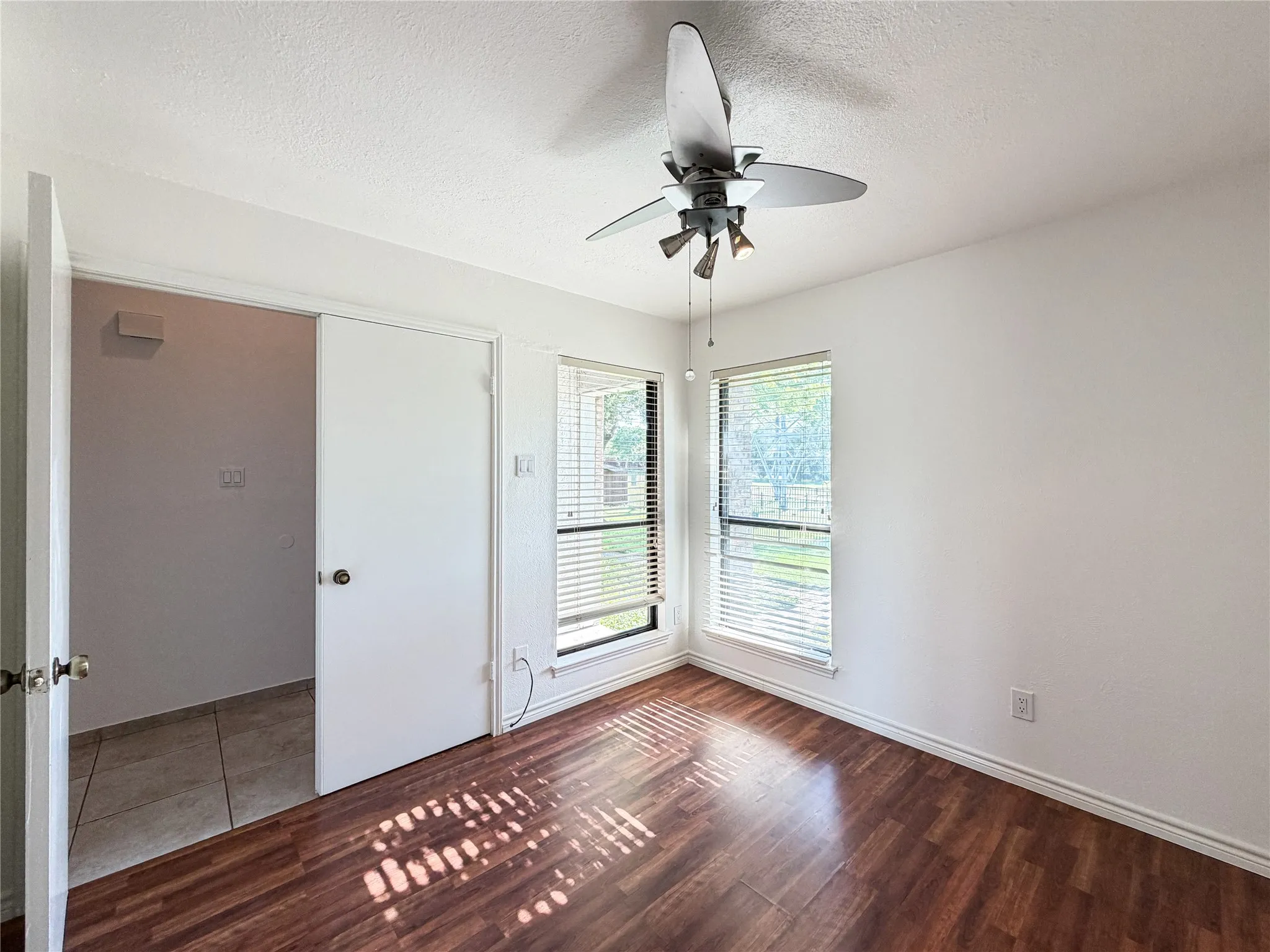 Wood-finish flooring, dual windows with blinds, ceiling fan with integrated lighting, and a closet with sliding doors