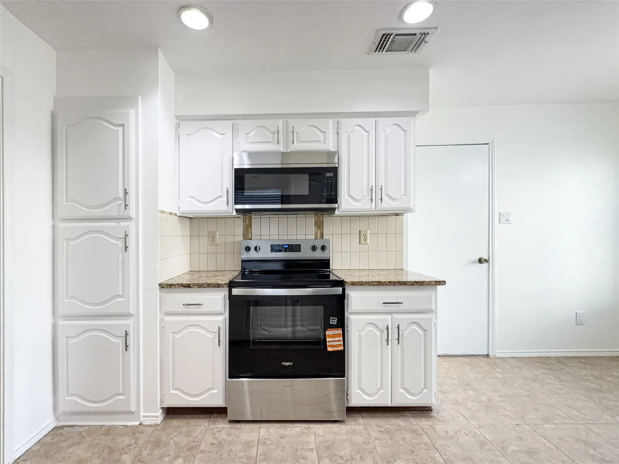 White cabinetry with granite-style countertops, stainless steel range and microwave, and tile flooring