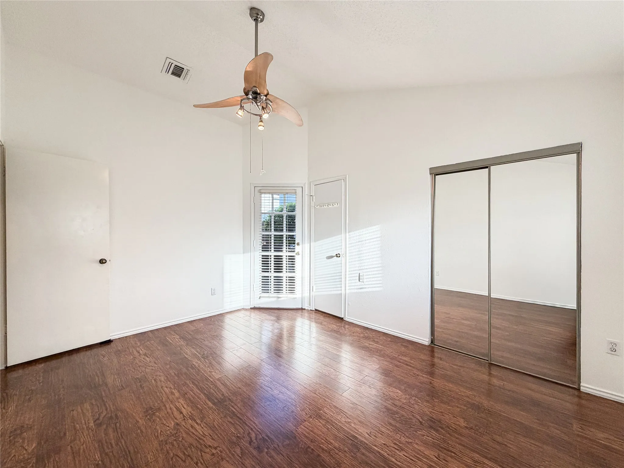 Wood-finish flooring, white walls, ceiling fan with integrated lighting, glass-paneled door, and mirrored closet doors