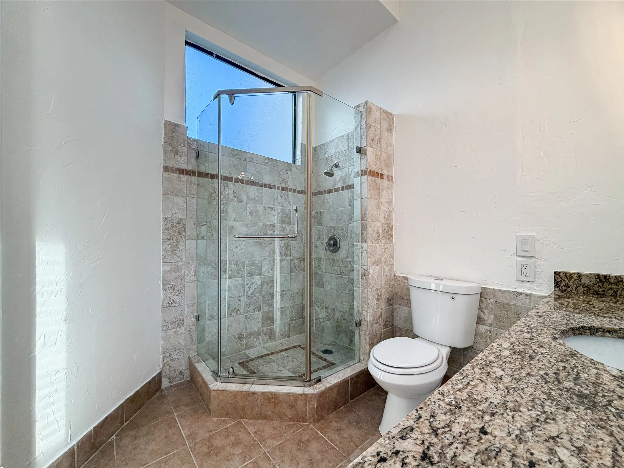 Corner glass-enclosed shower with tile surround, built-in shower niche, and an upper transom window