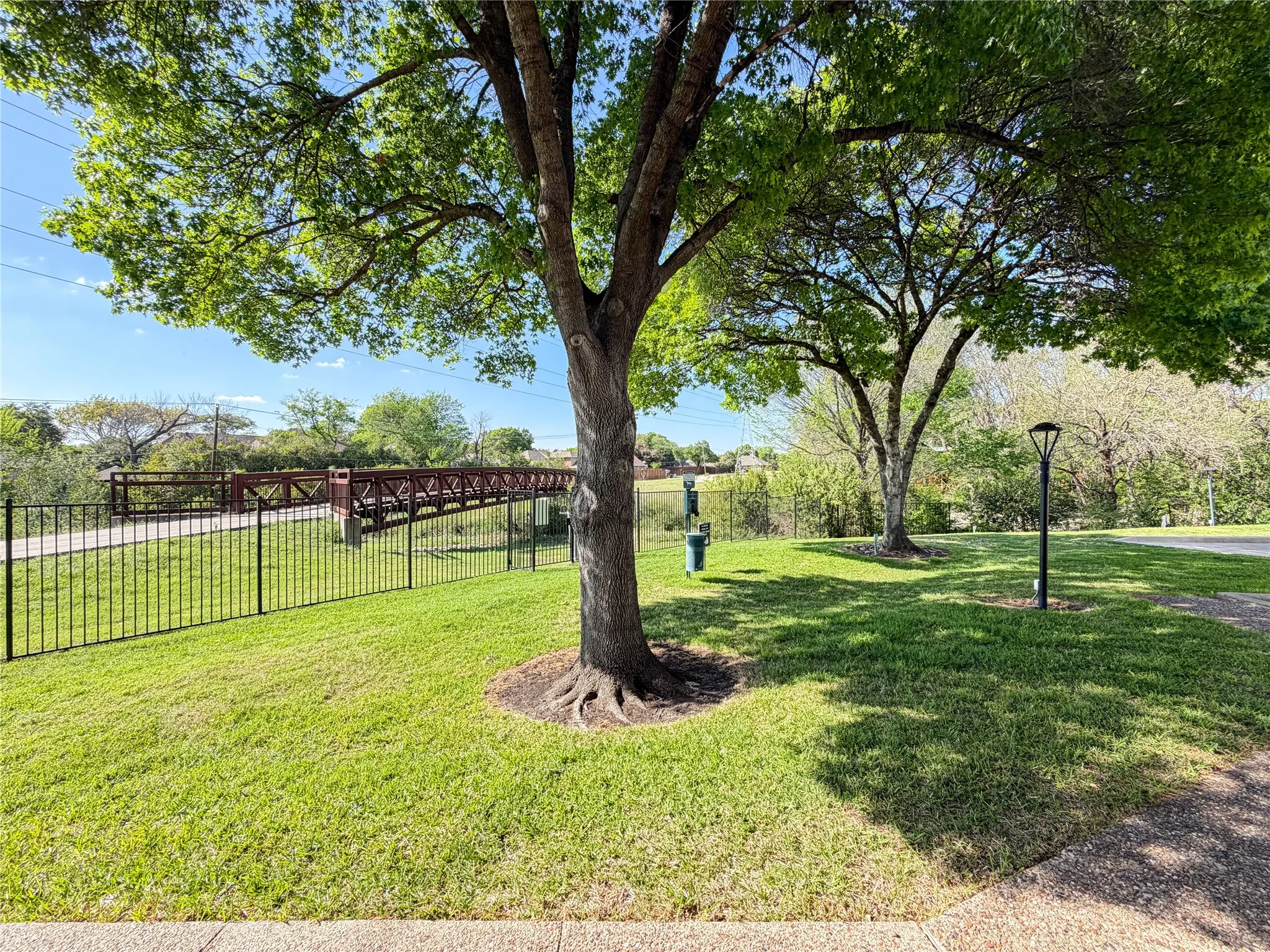 Manicured lawn with mature trees and a walking path, featuring a black wrought iron fence